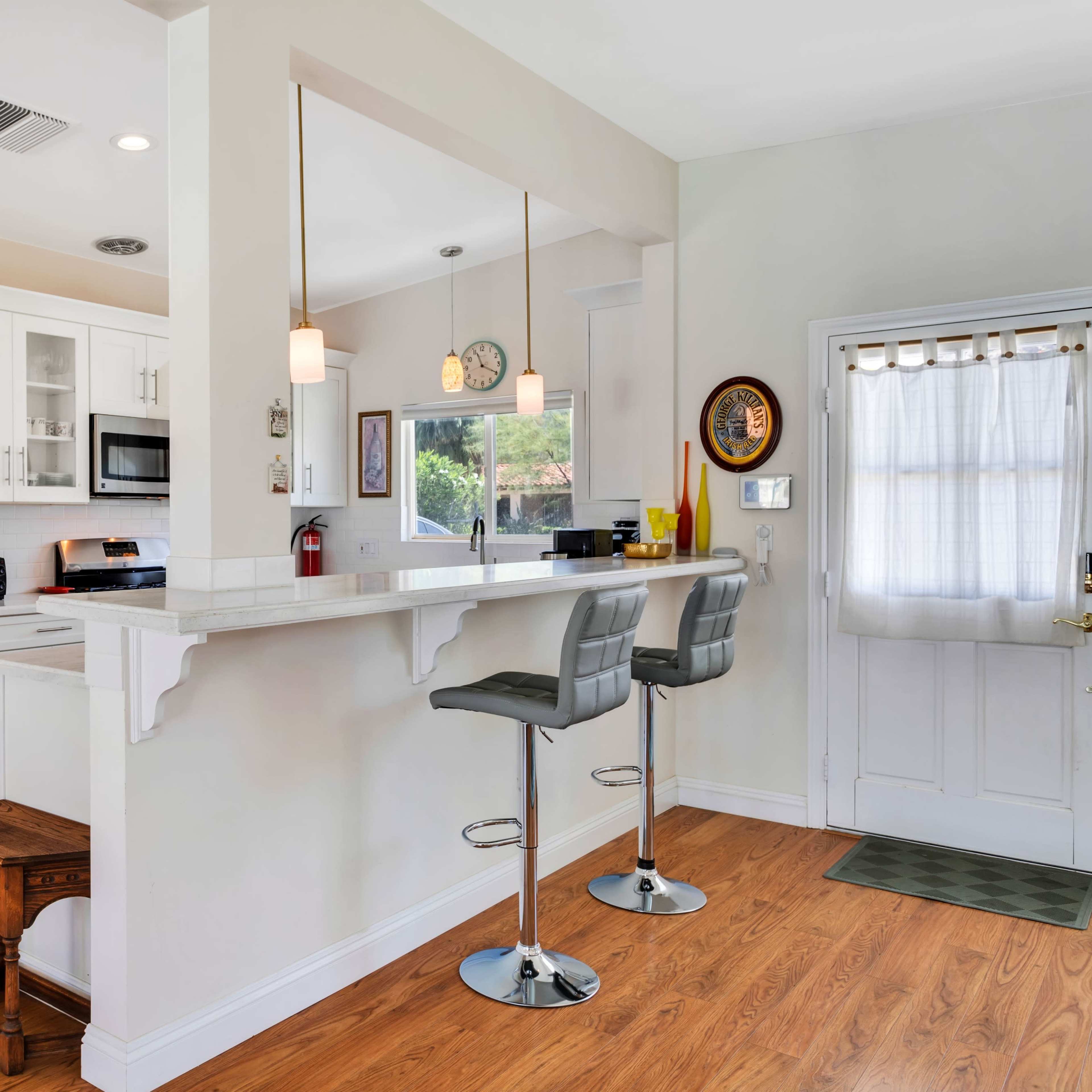 A modern kitchen with a stainless steel refrigerator, white cabinetry, and a bar area with two stools.
