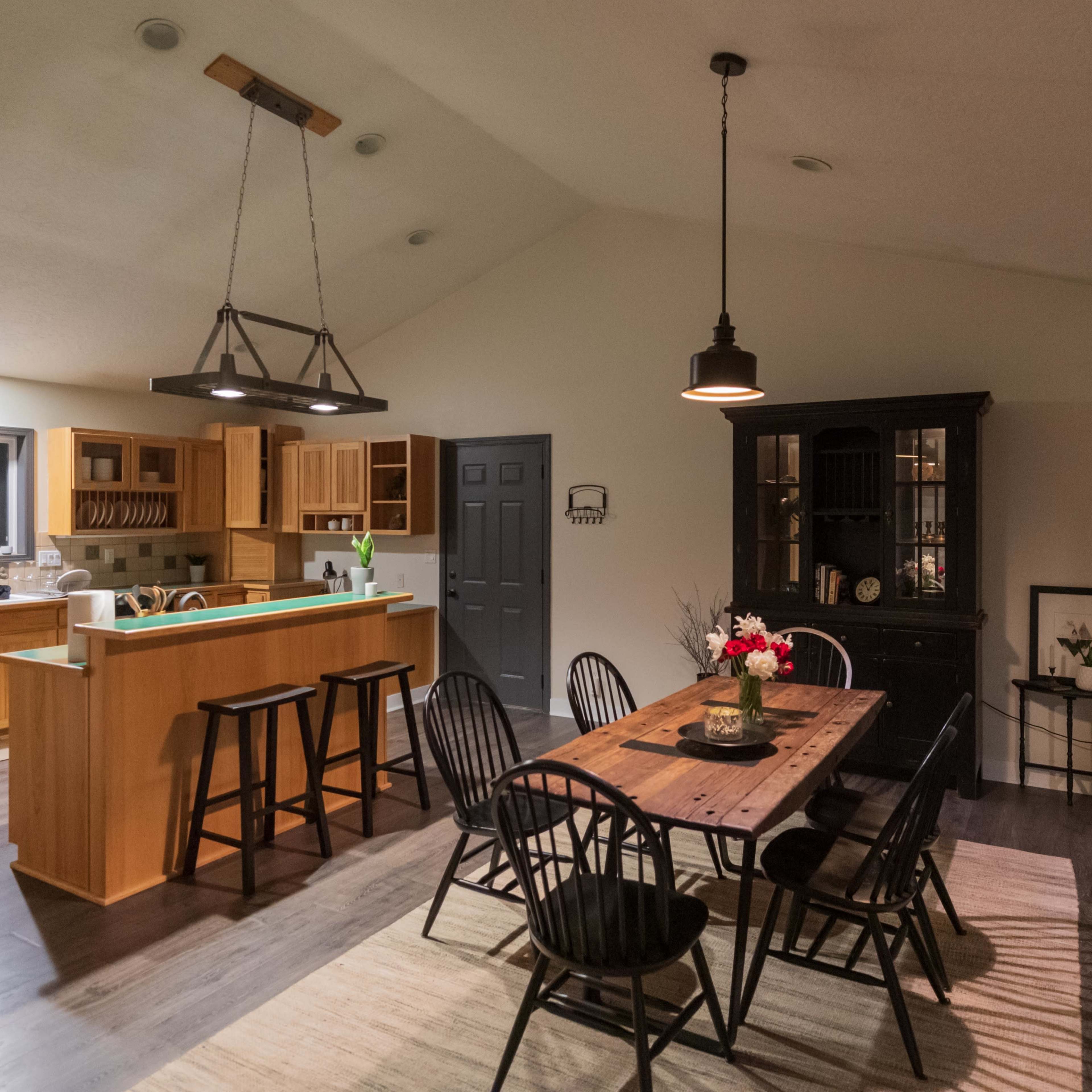 A modern kitchen and dining area feature wooden cabinetry, a large dining table, and black chairs.