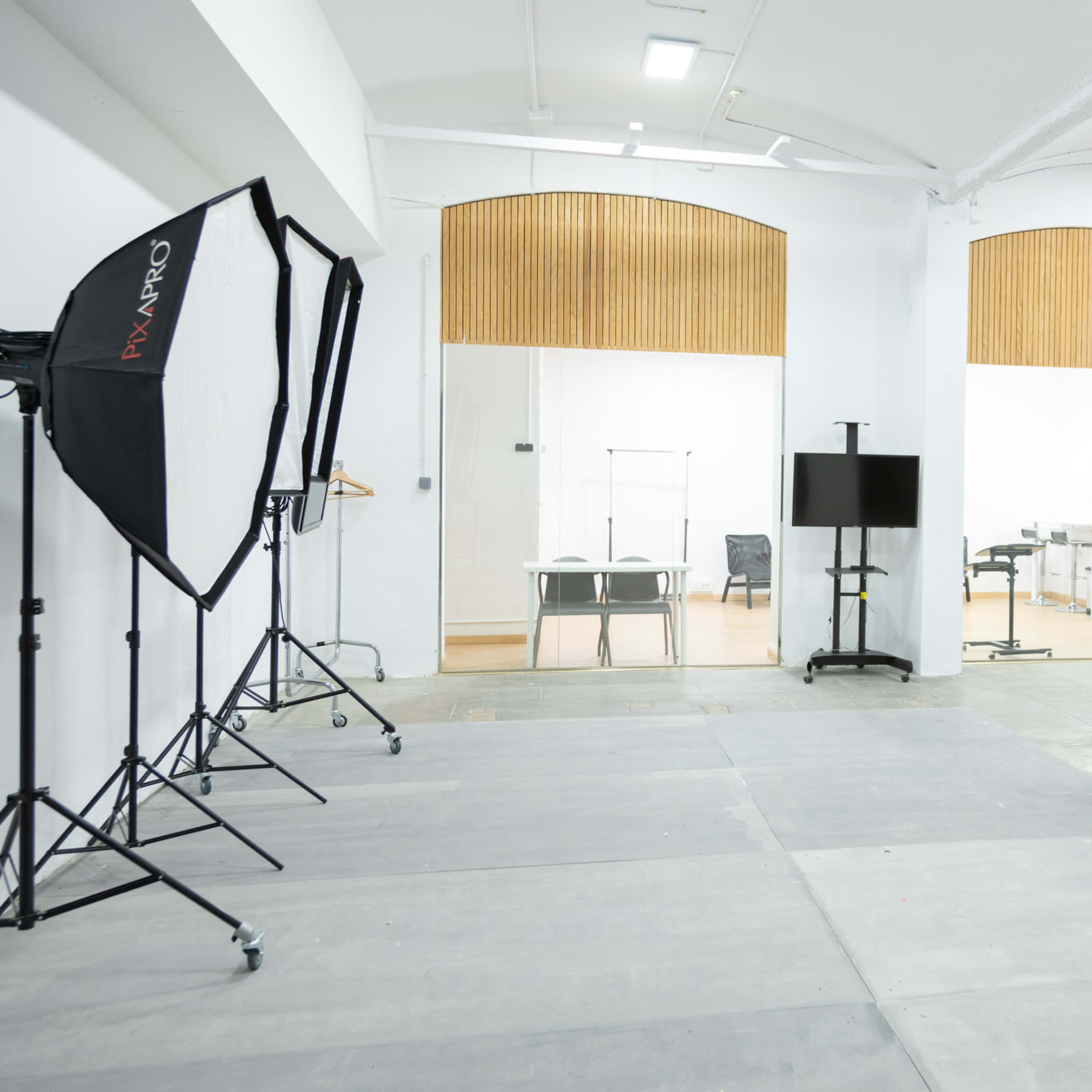 A spacious, empty studio with photography equipment on the left and an office area with wooden panels in the background.