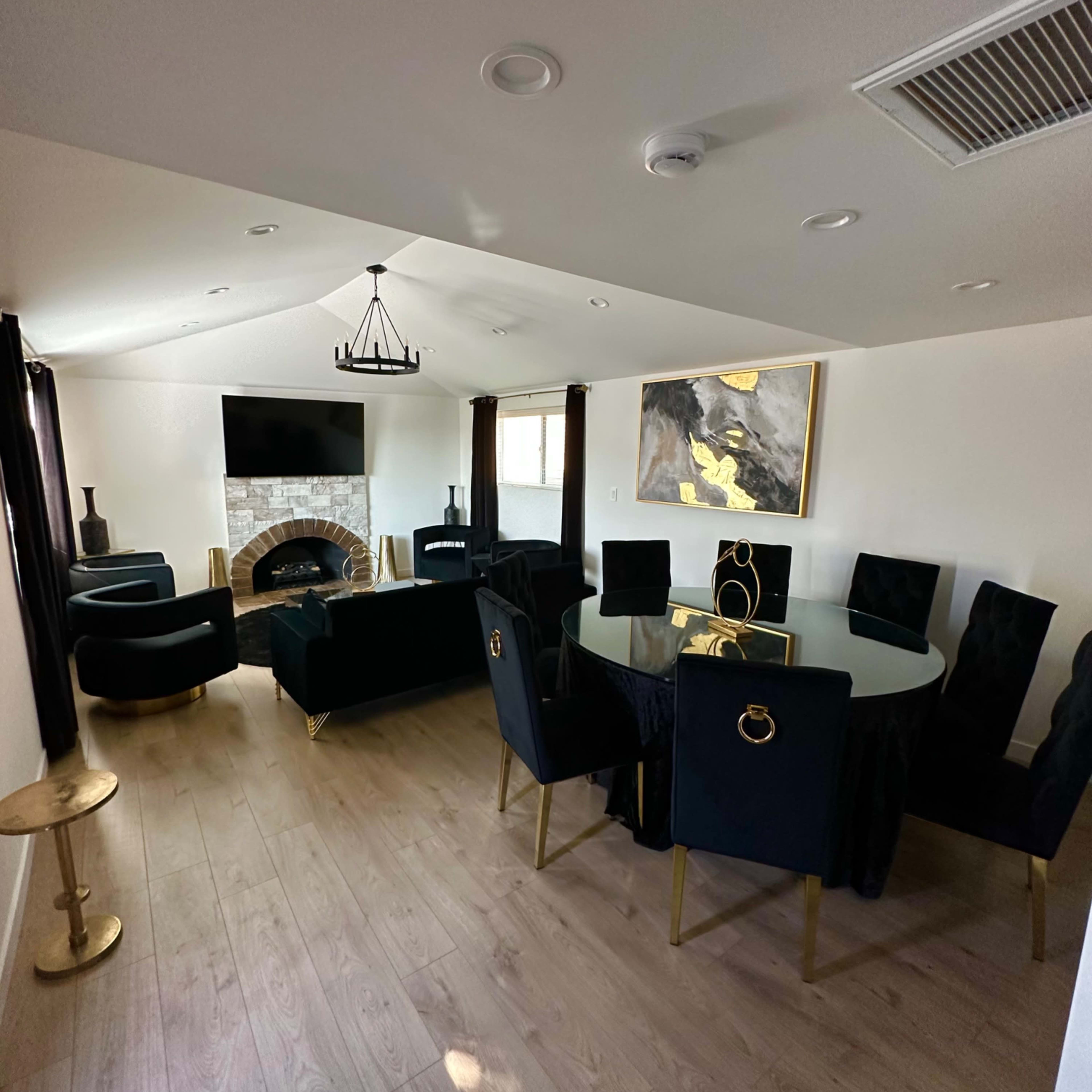 A modern living room features a black seating area, a circular dining table, a fireplace, and an artwork on the wall.