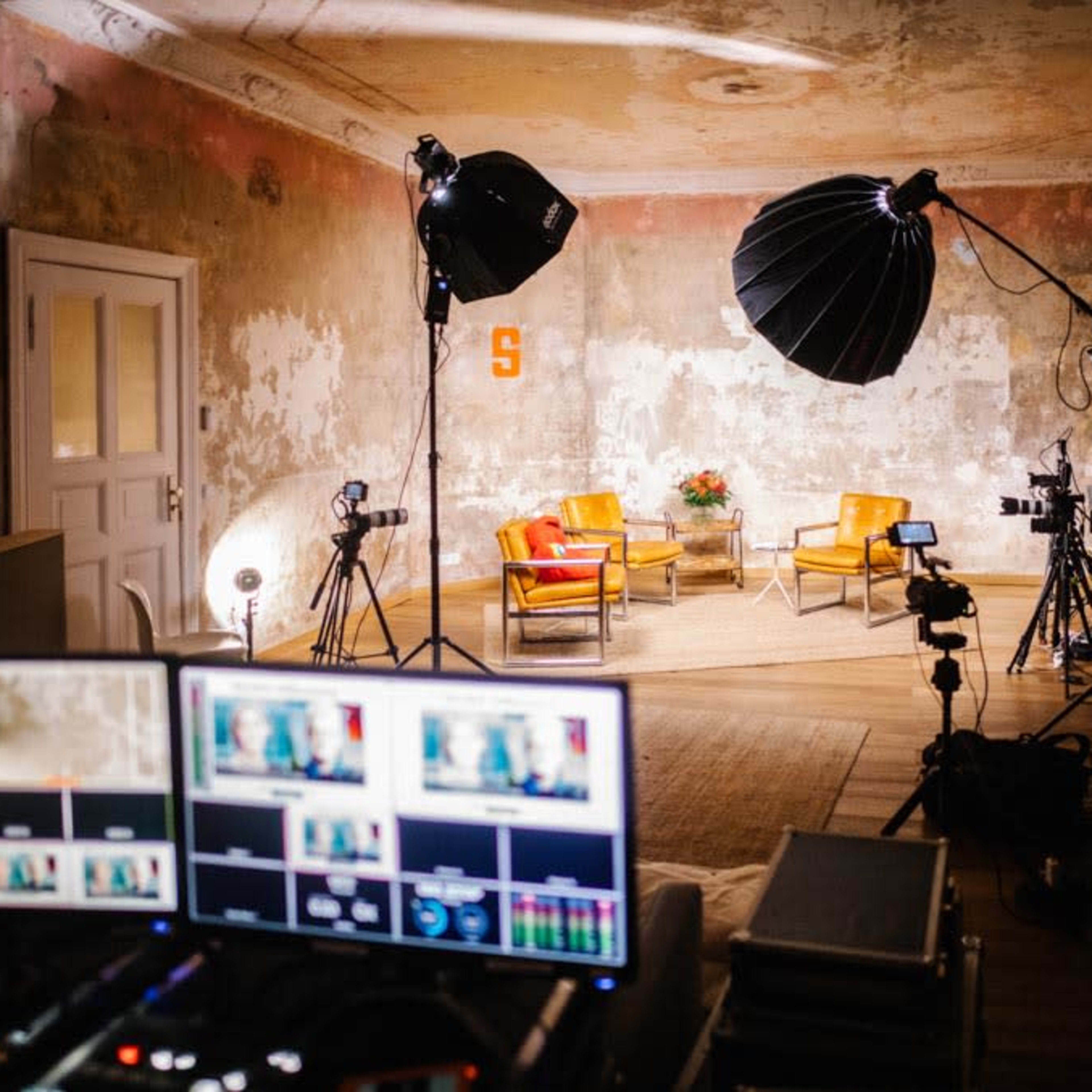 A well-equipped video production studio featuring two yellow chairs and various lighting and camera equipment in a rustic room.