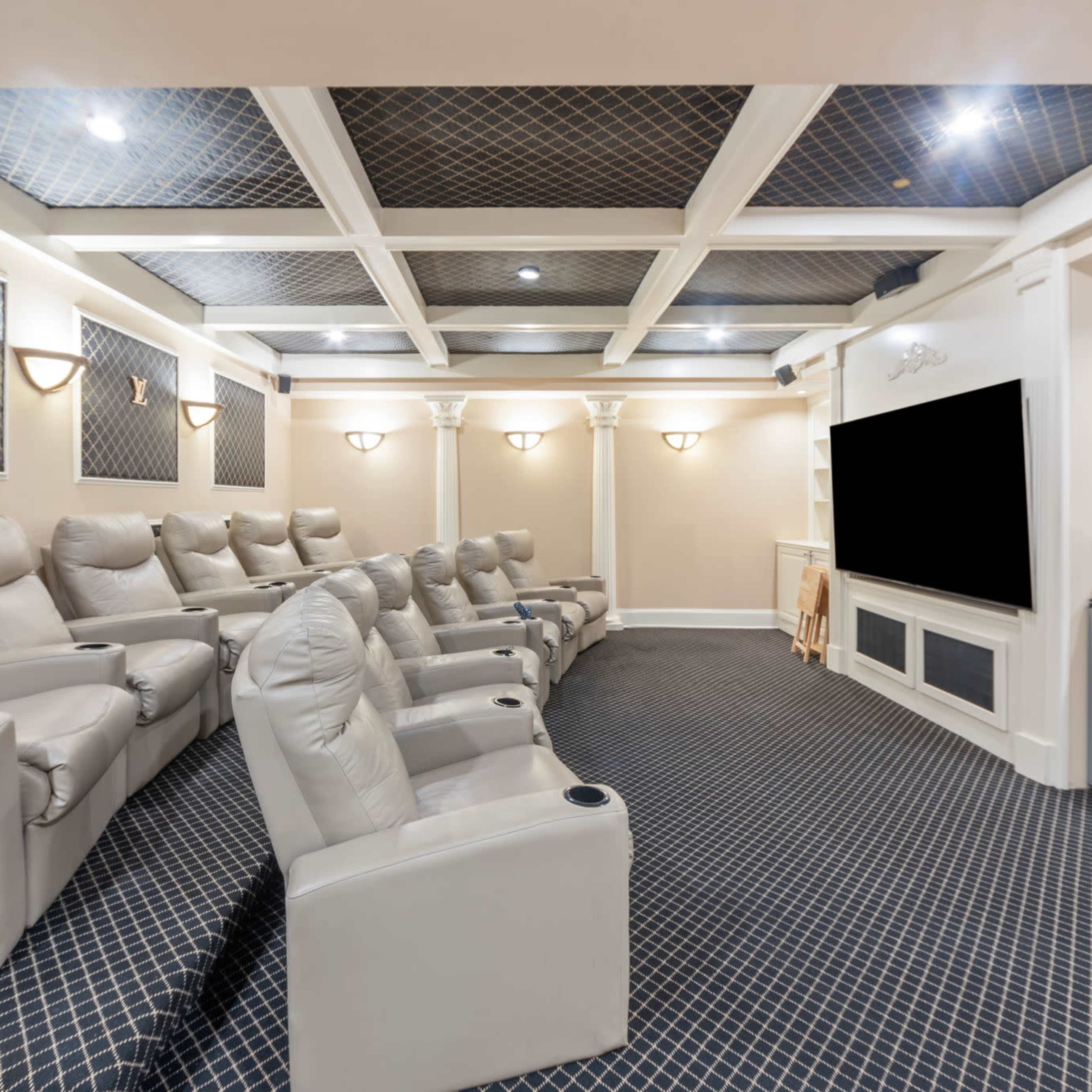 A home theater with reclining leather chairs arranged in rows facing a large black screen, set within a well-lit room featuring decorative paneling.