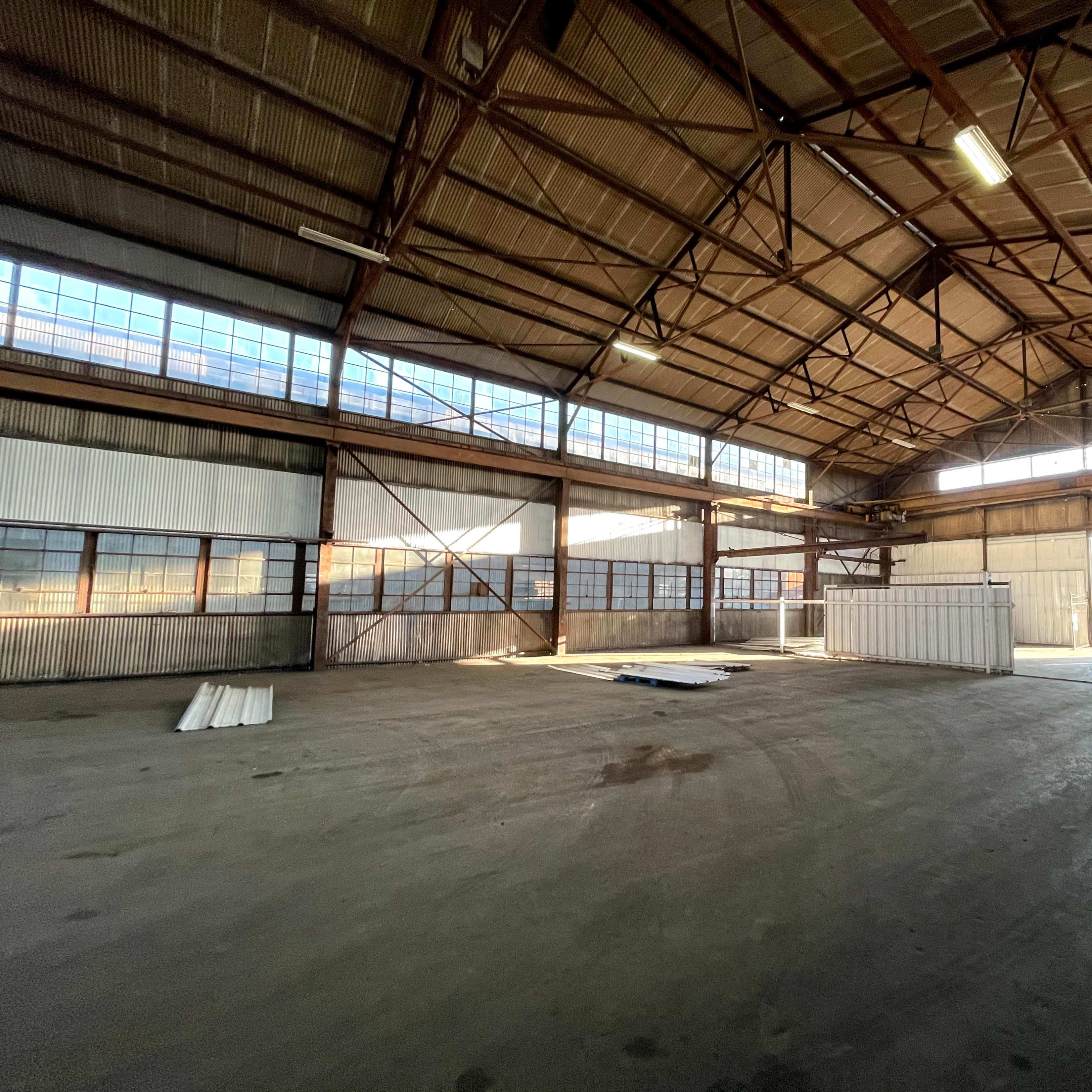 A large, empty industrial warehouse with high ceilings and large windows allowing natural light to enter.