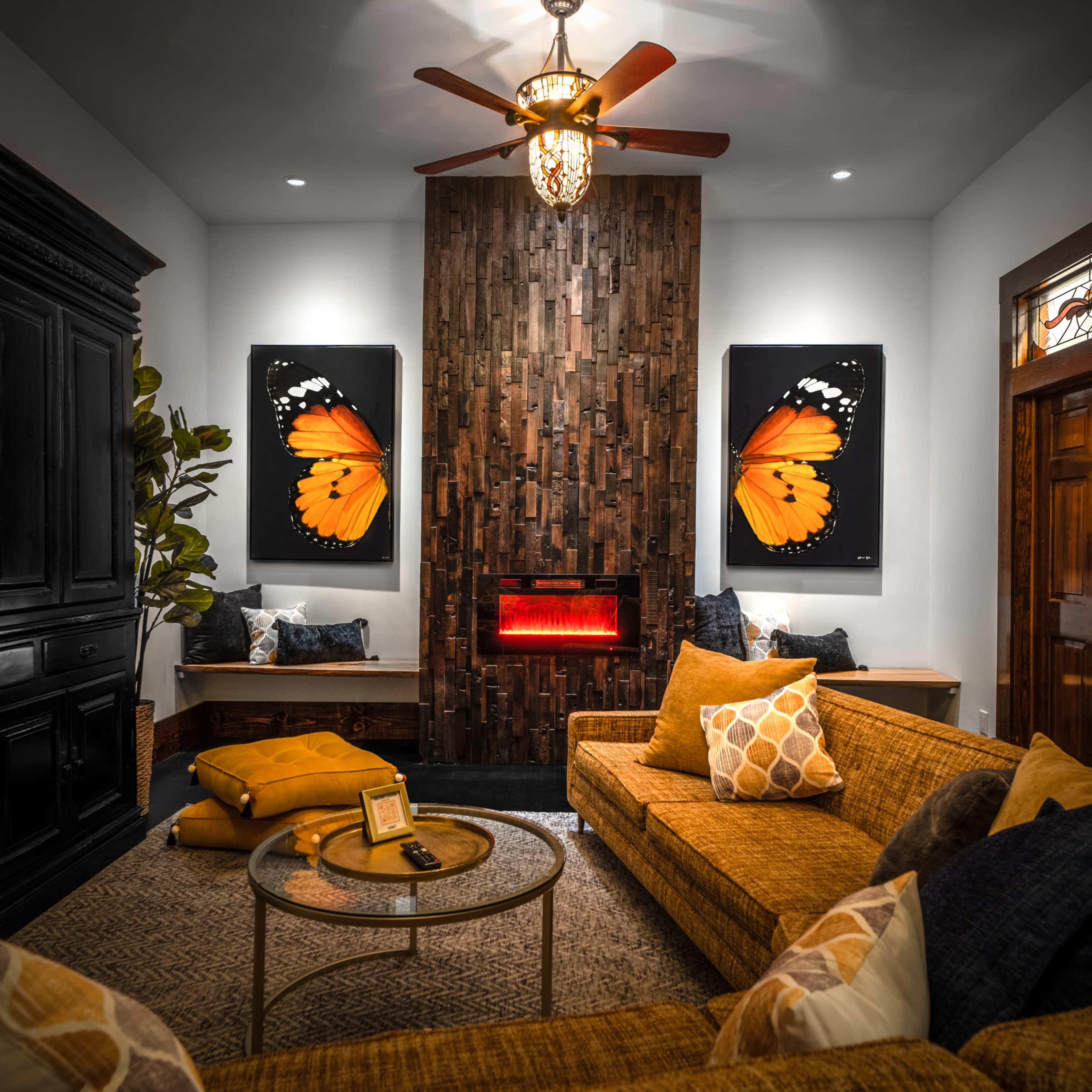 The living room features a cozy arrangement with a brown sectional sofa, a round coffee table, and large butterfly artwork on a wooden accent wall, complemented by a modern electric fireplace.