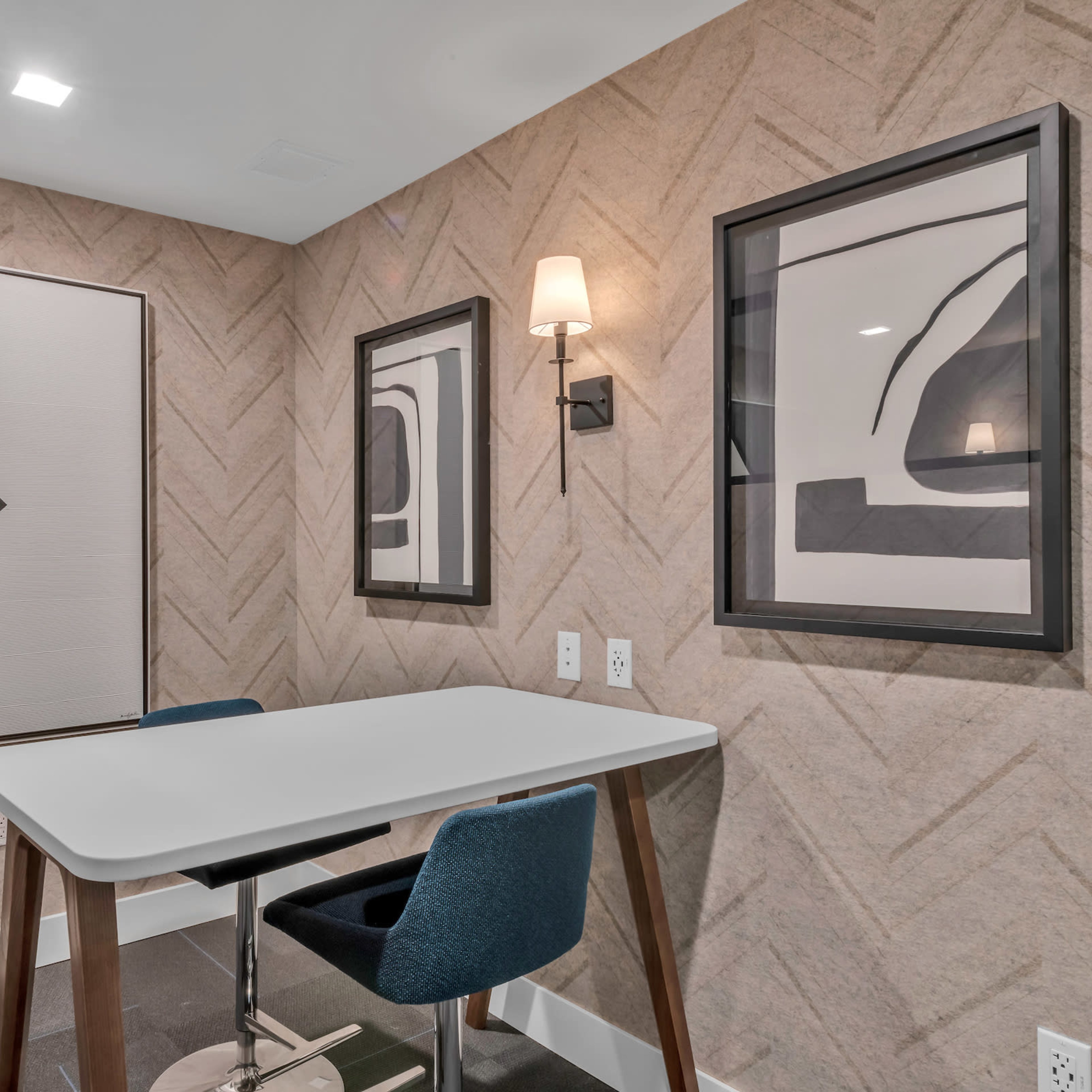 A small room featuring a table with two chairs, flanked by two framed abstract artworks on the textured wall.