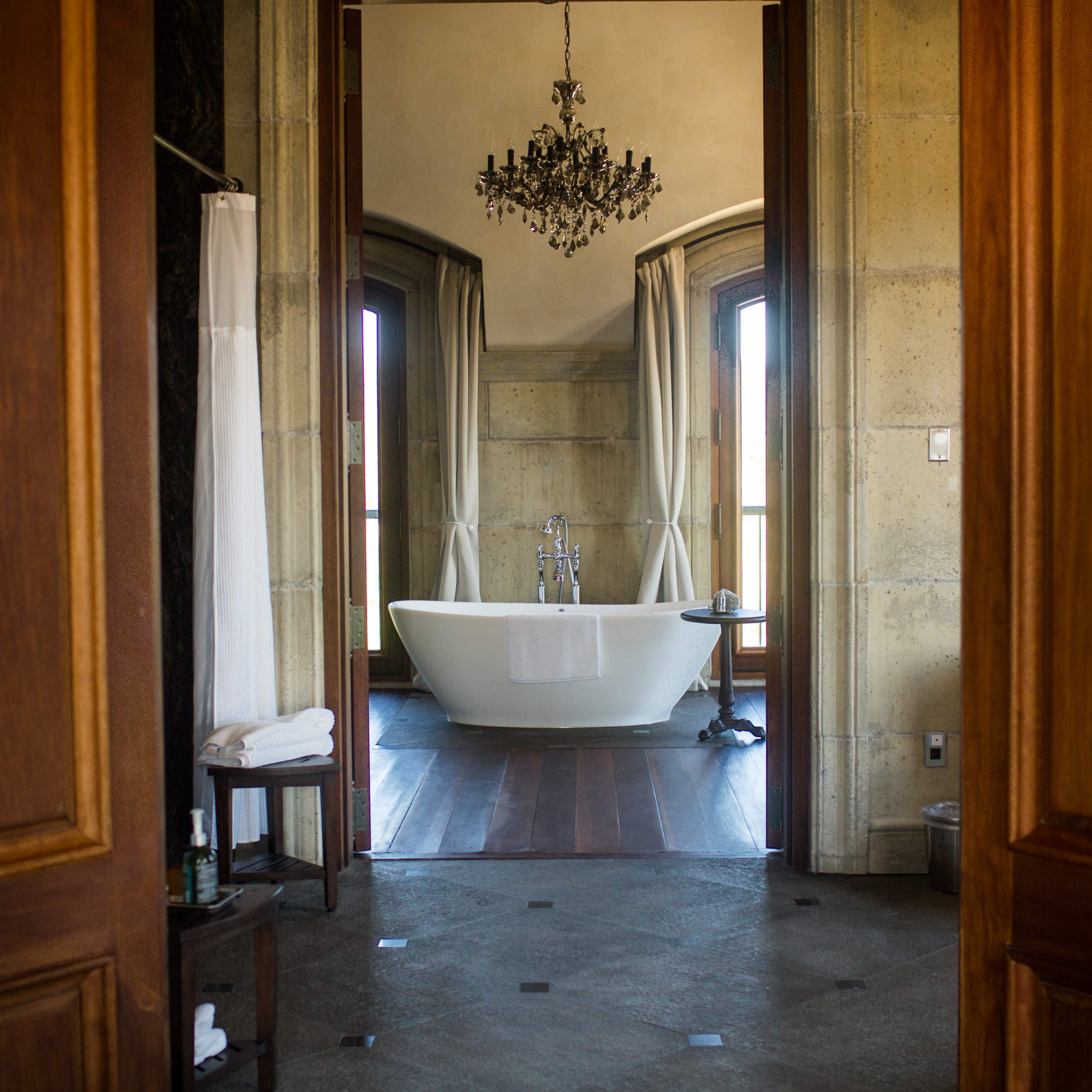 A spacious bathroom features a freestanding bathtub and large windows, framed by elegant curtains.