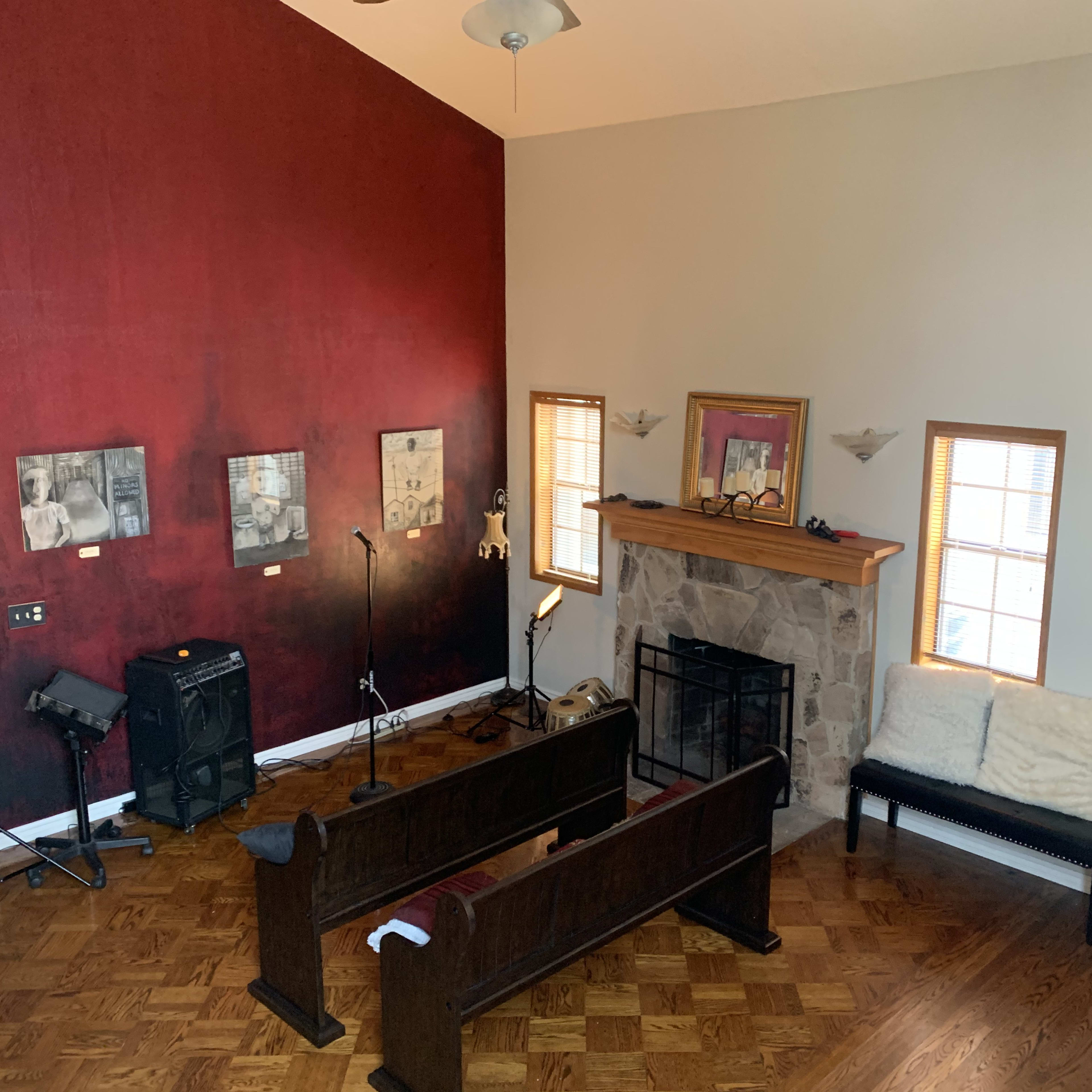 A spacious living room with a high ceiling, featuring a red accent wall, a stone fireplace, wooden benches, and various pieces of artwork displayed on the walls.