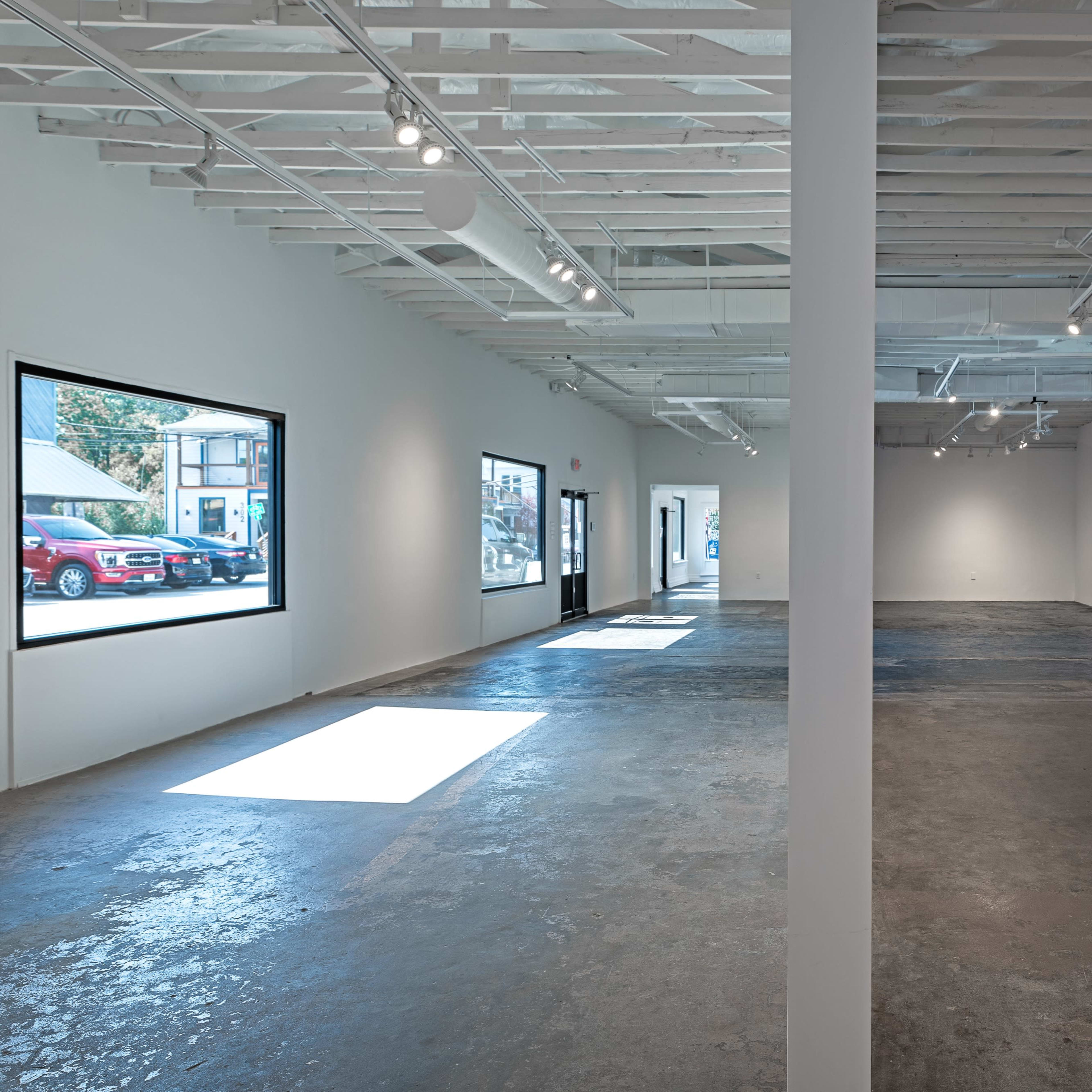 A spacious, empty art gallery with a polished concrete floor, exposed beams, and large windows allowing natural light to enter.