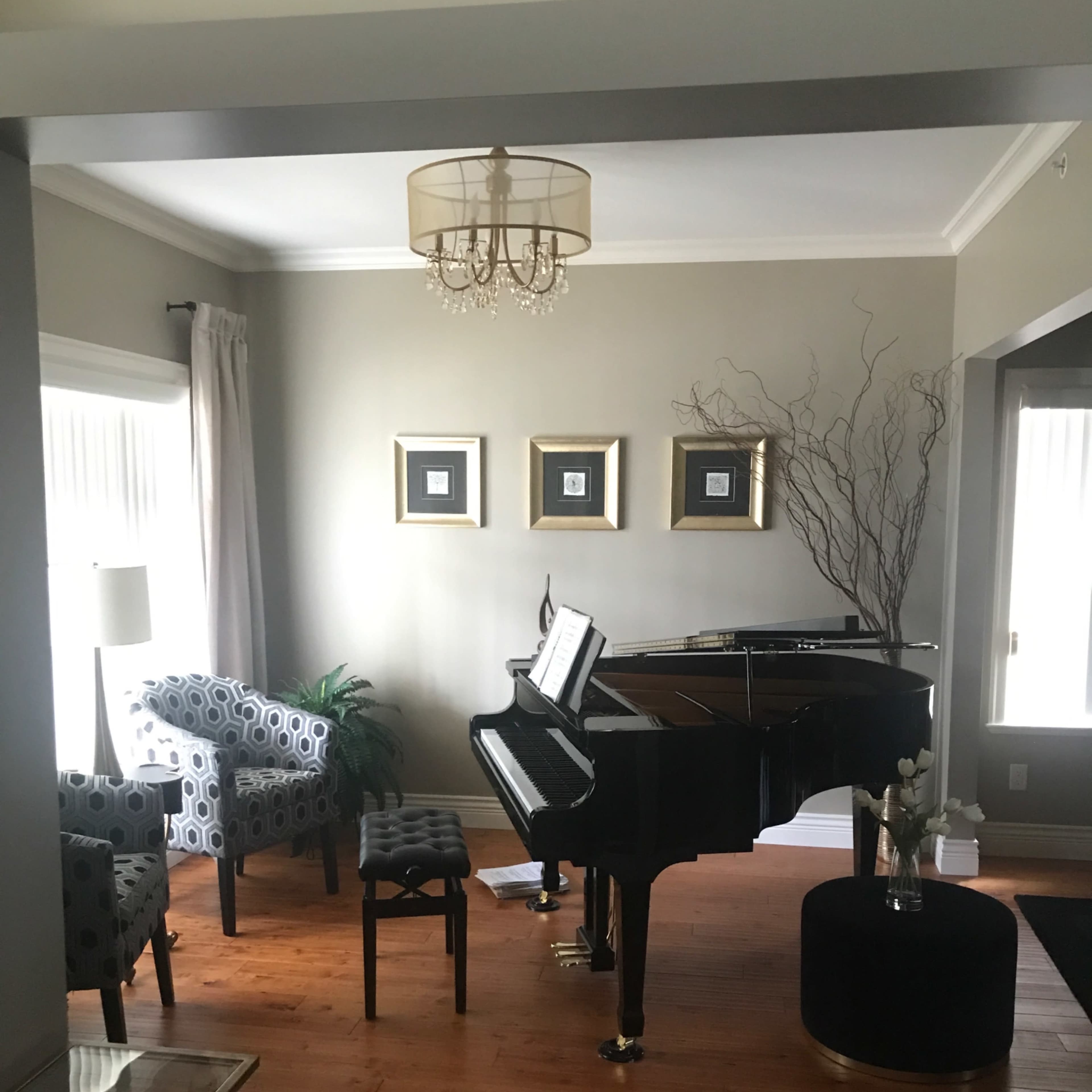 The room features a grand piano, a pair of upholstered chairs, and wall art above a small table, all set on polished wooden flooring.