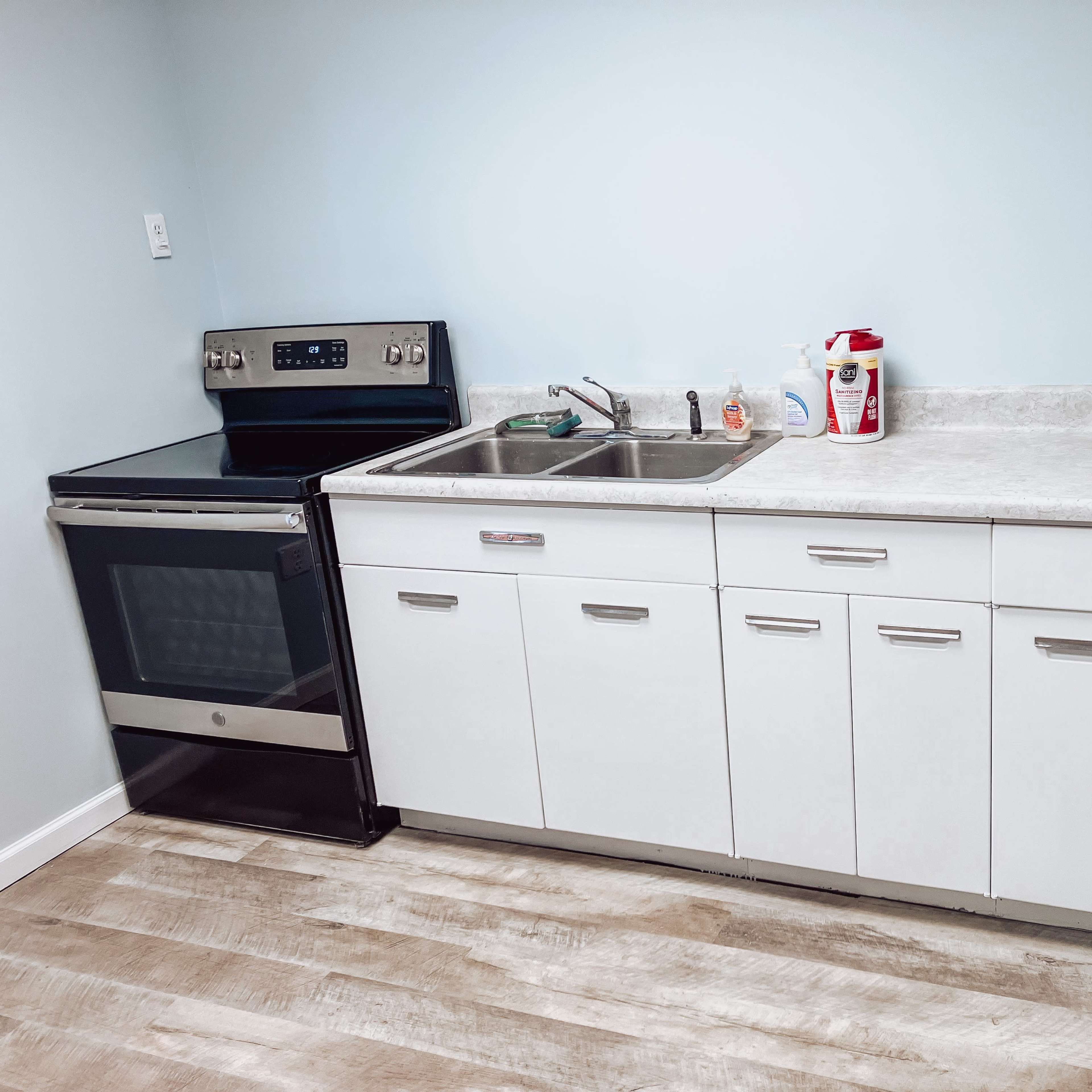 A clean kitchen area with a stainless steel oven, a double sink, and white cabinets situated against a light blue wall.