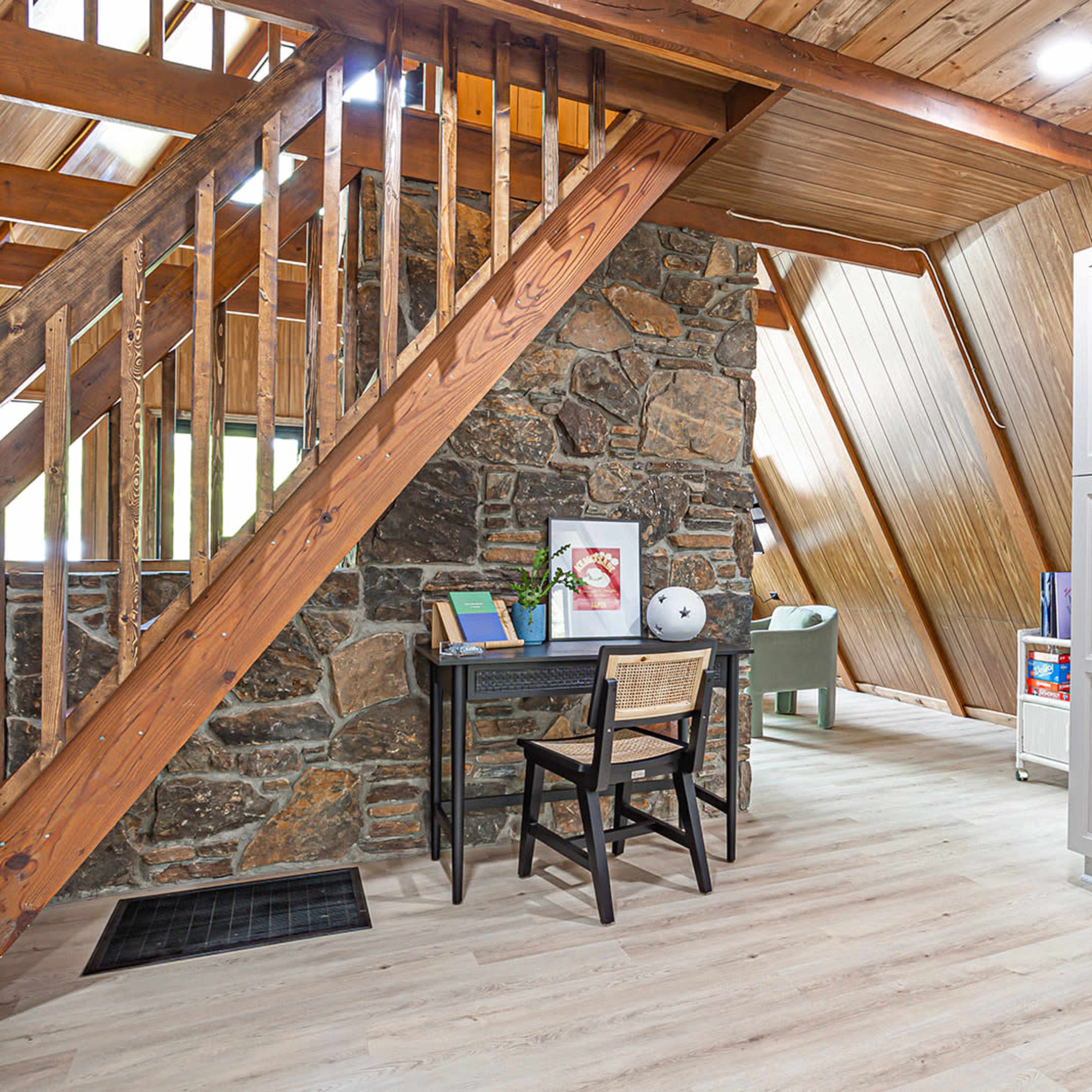 A kitchen area with a stainless steel refrigerator, a wooden staircase, and a stone wall leading to a room with slanted wooden walls.