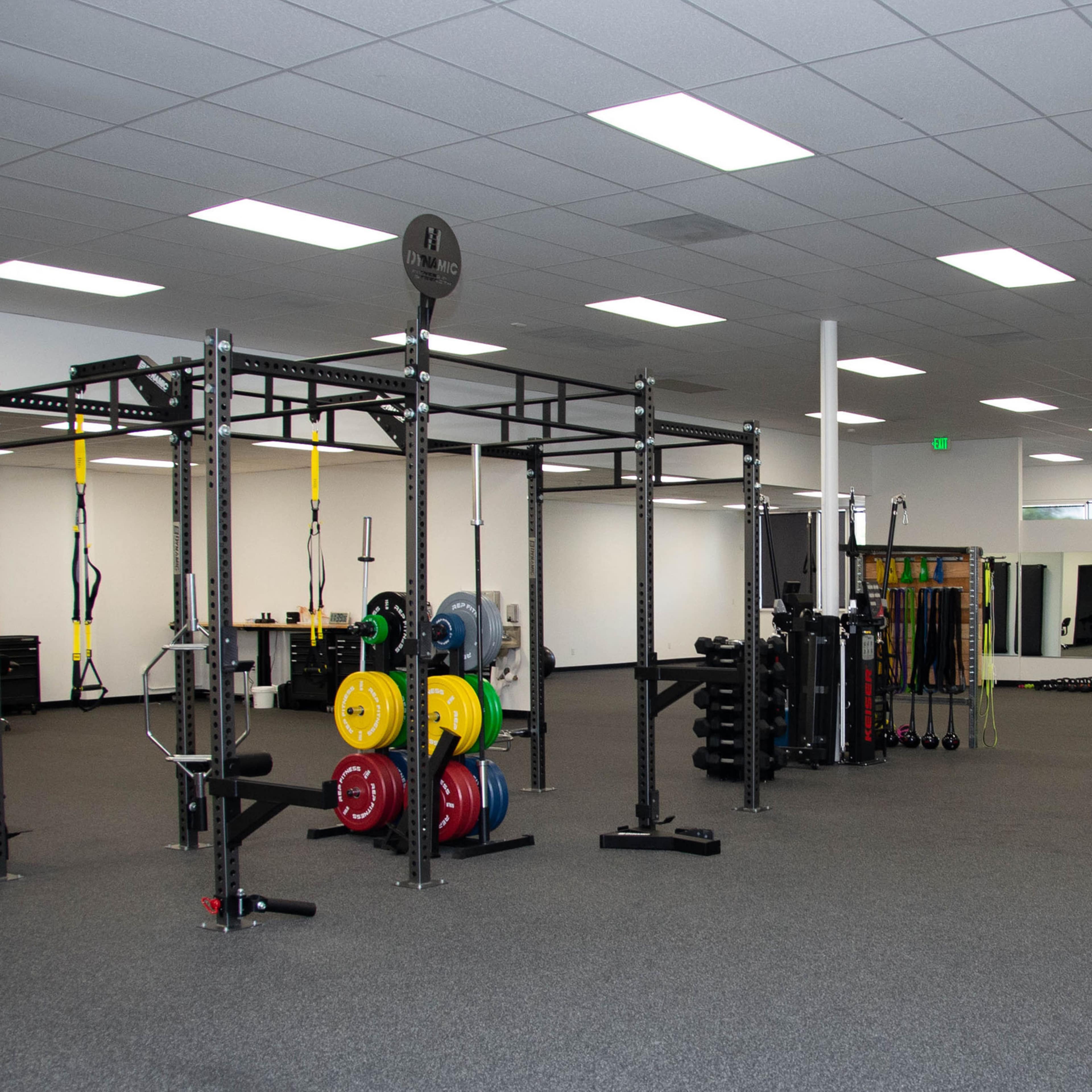 A well-equipped gym featuring a weightlifting rack, various weights, and exercise equipment in a spacious, brightly lit area.