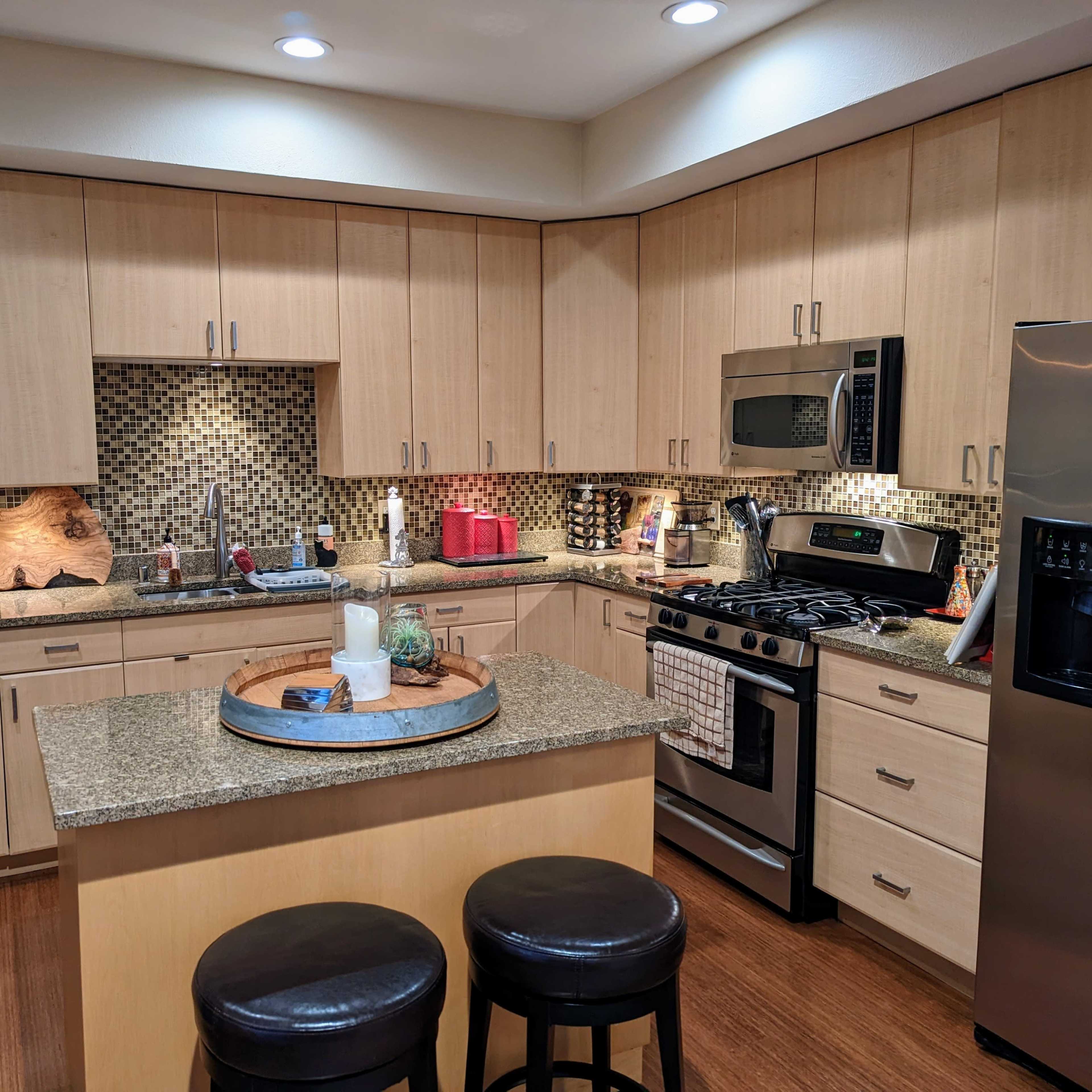 A modern kitchen featuring wooden cabinets, stainless steel appliances, a granite countertop, and a mosaic tile backsplash.
