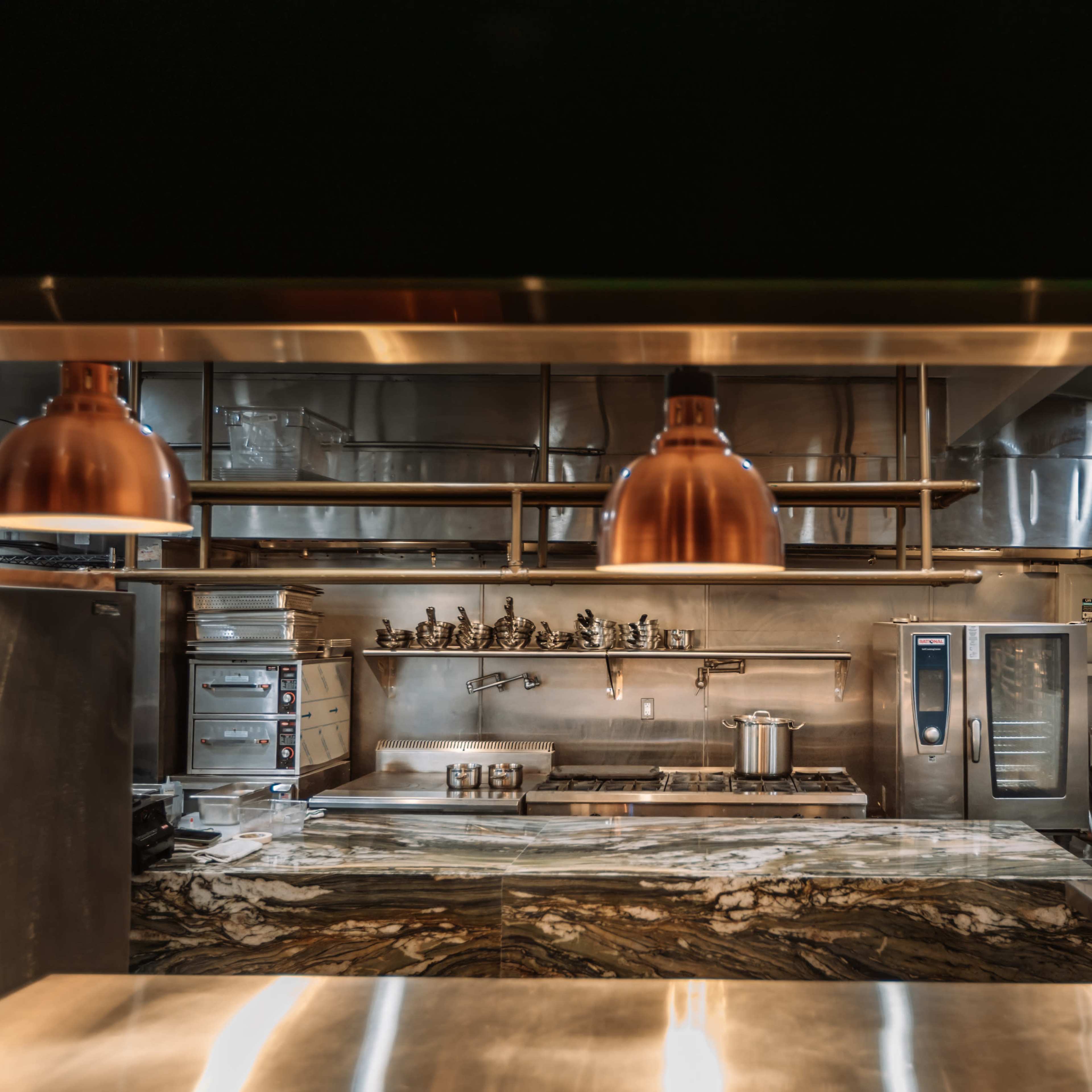 A modern kitchen features a marble countertop, stainless steel appliances, and copper pendant lights.