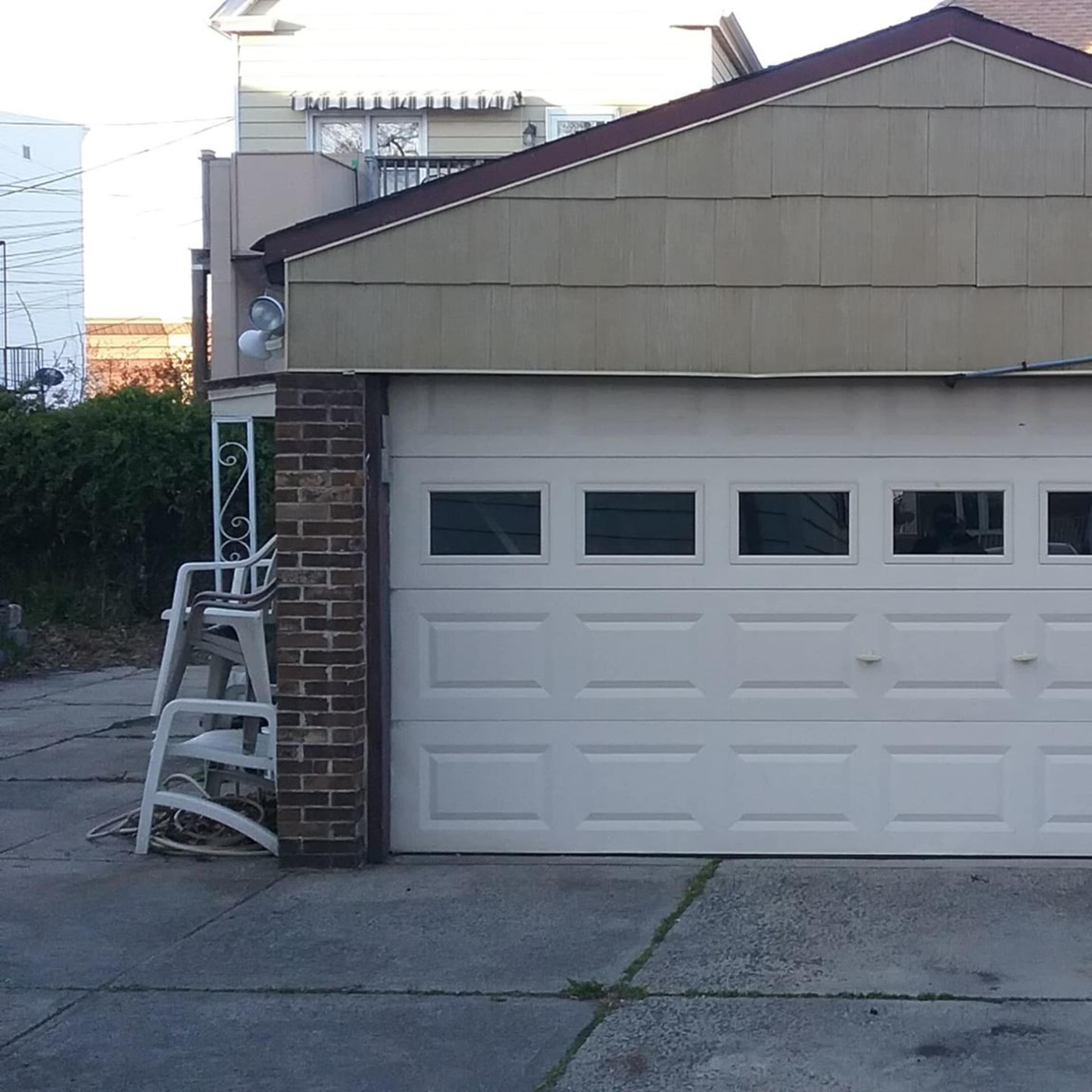 A closed garage door with five rectangular windows at the top, set in a brick and siding structure.