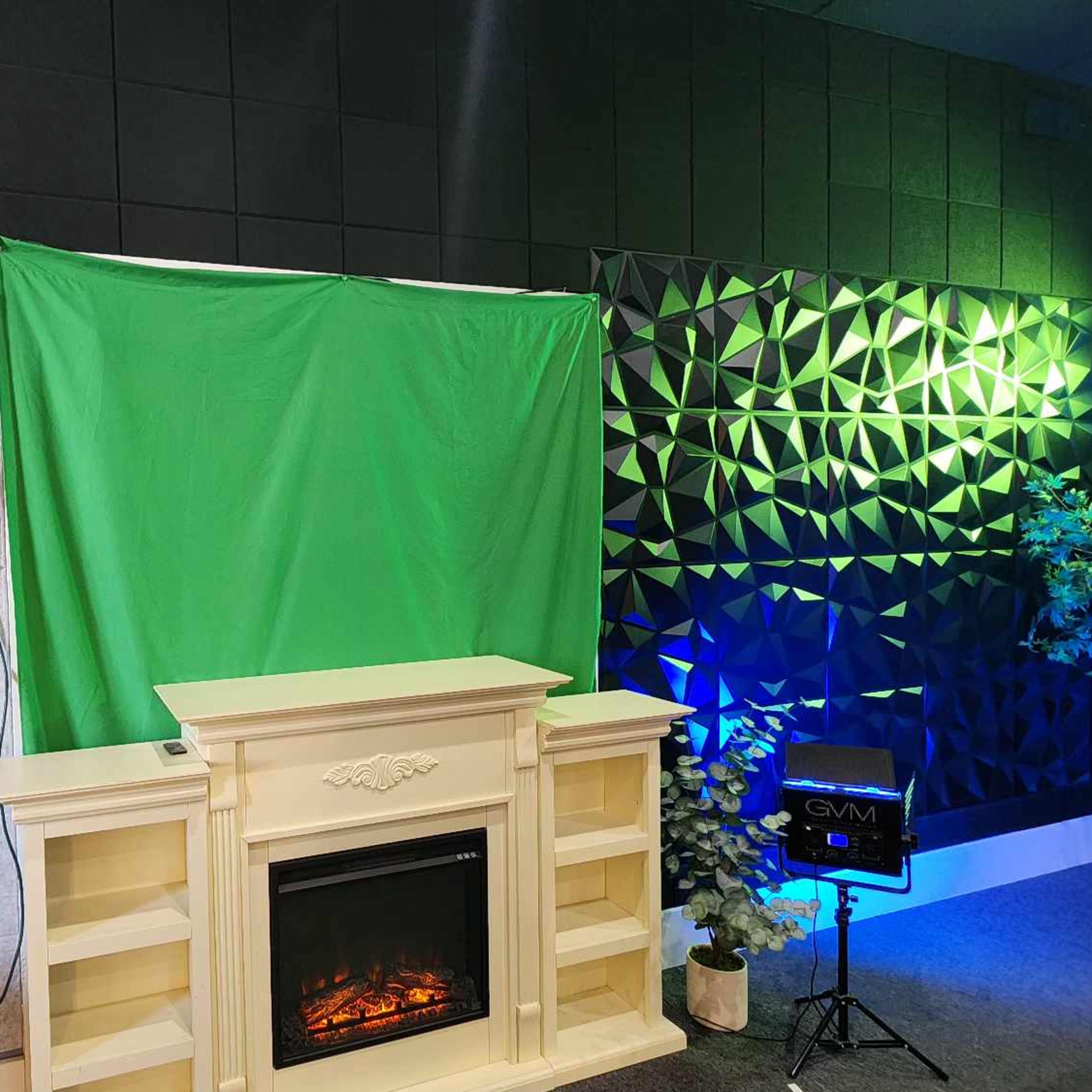 A green screen is set up in front of a decorative fireplace, flanked by textured black and gray walls with ambient lighting.