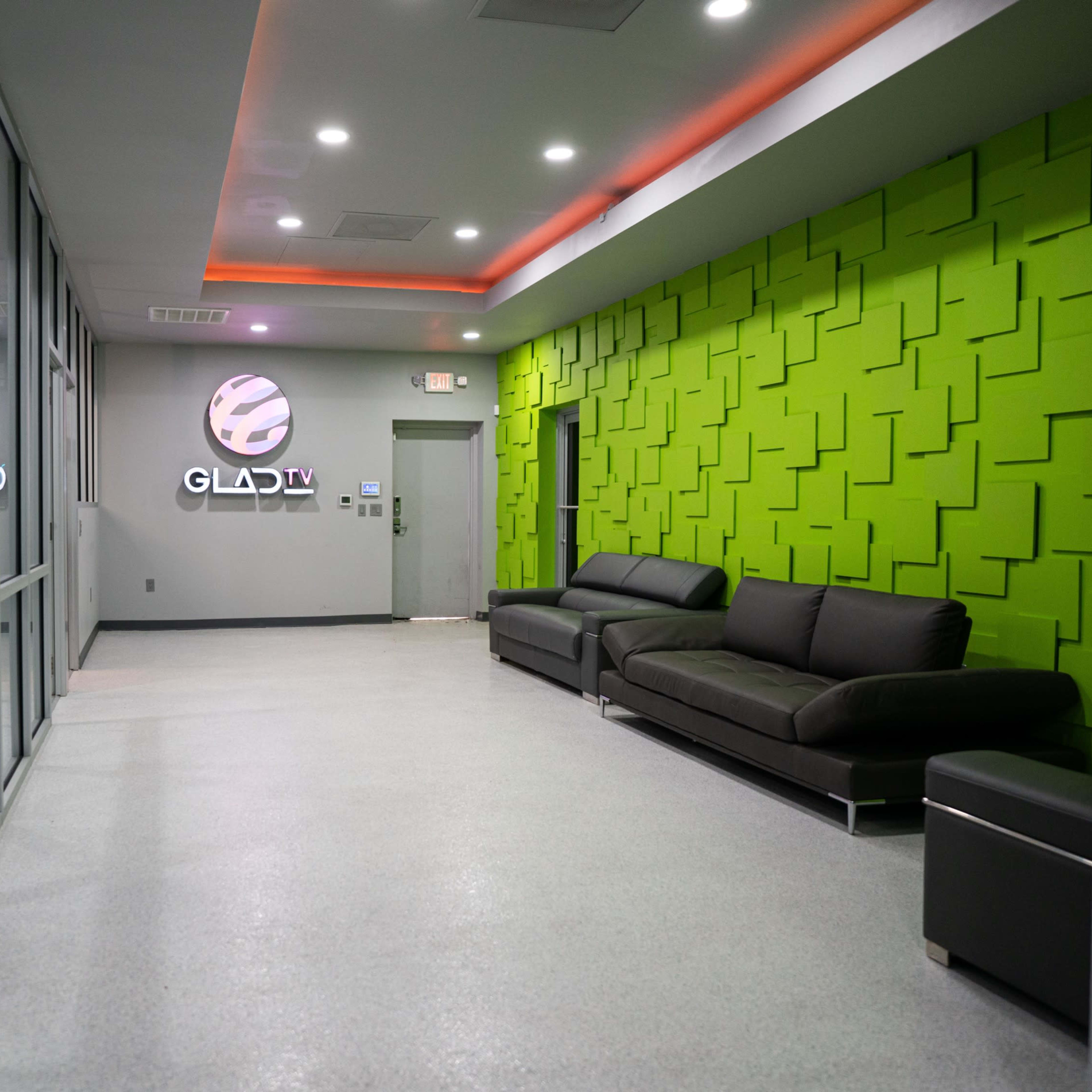 A modern lobby area with a green textured wall, a black sofa, and large glass windows.