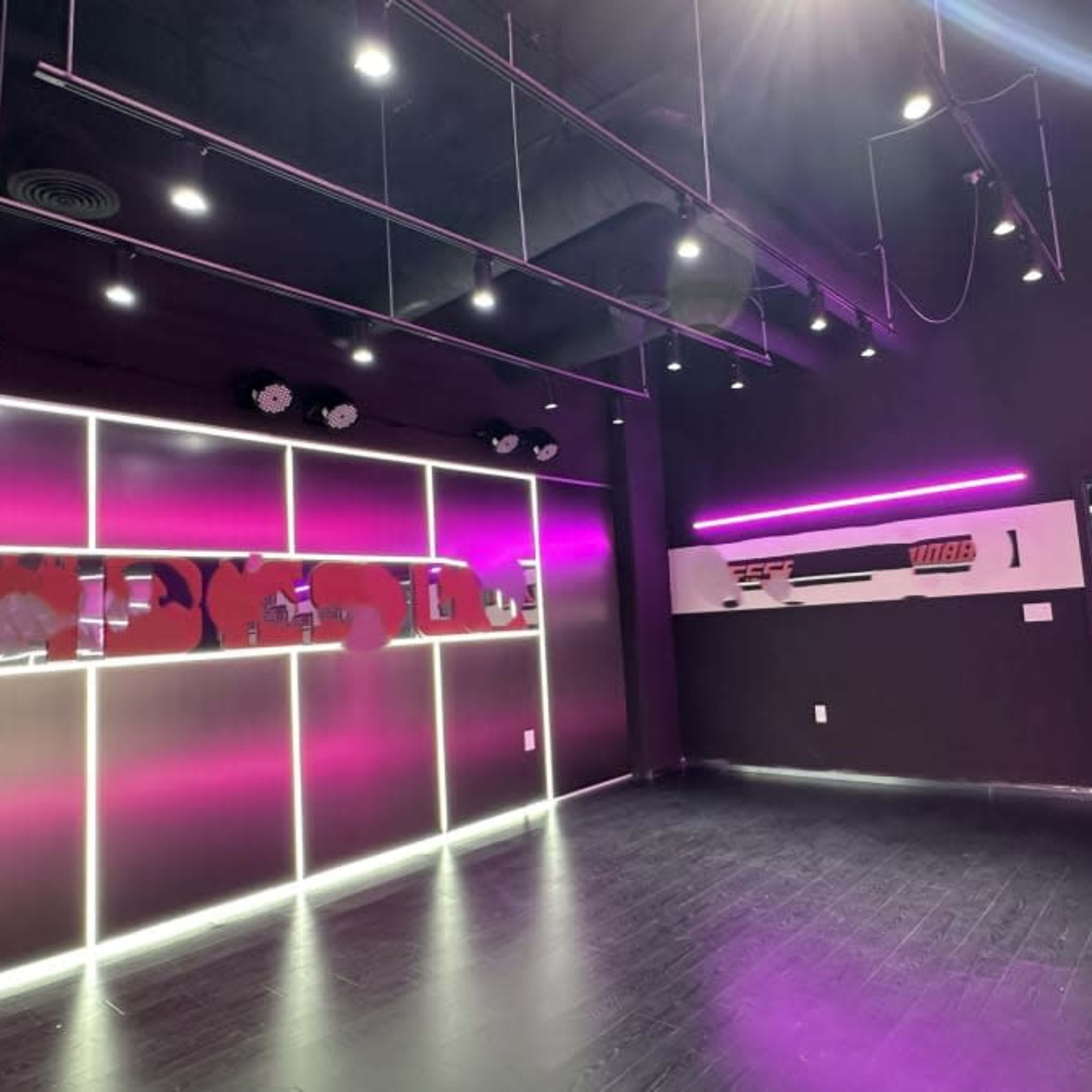 A modern fitness studio with black walls, pink neon lighting, and a mirrored wall.