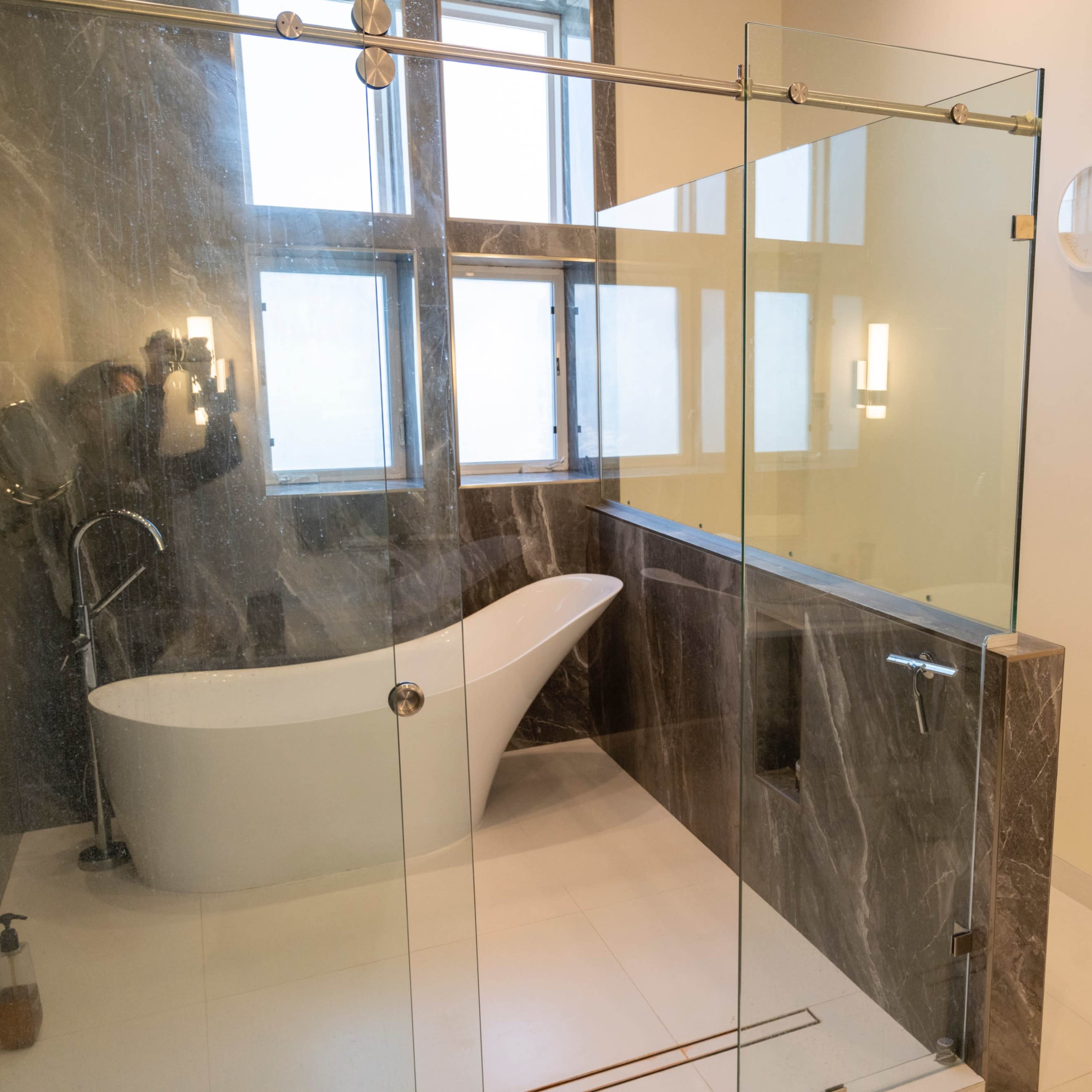 A modern bathroom featuring a glass shower enclosure, a freestanding tub, and large windows that let in natural light.