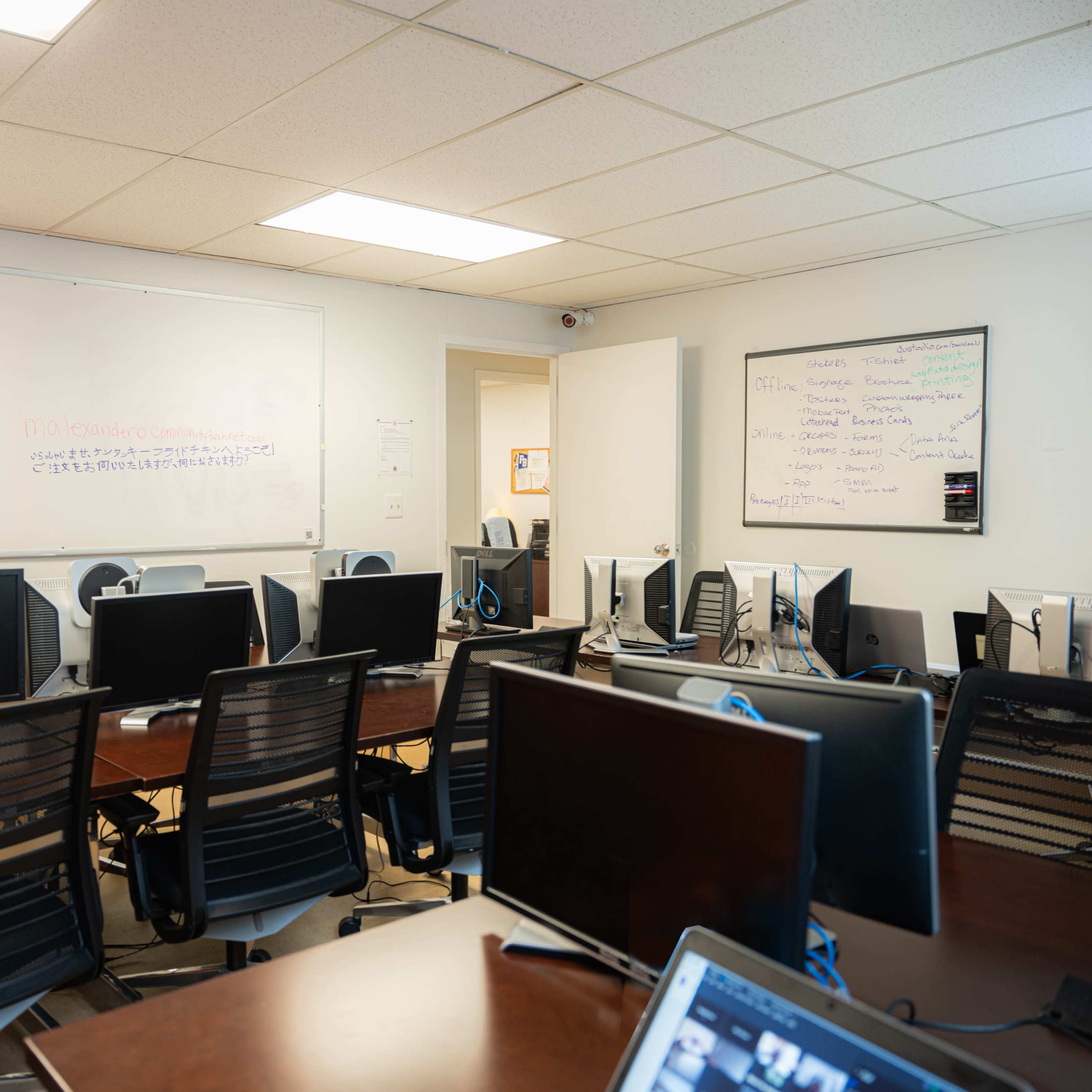 A busy office space with multiple desks equipped with computers and whiteboards on the walls.