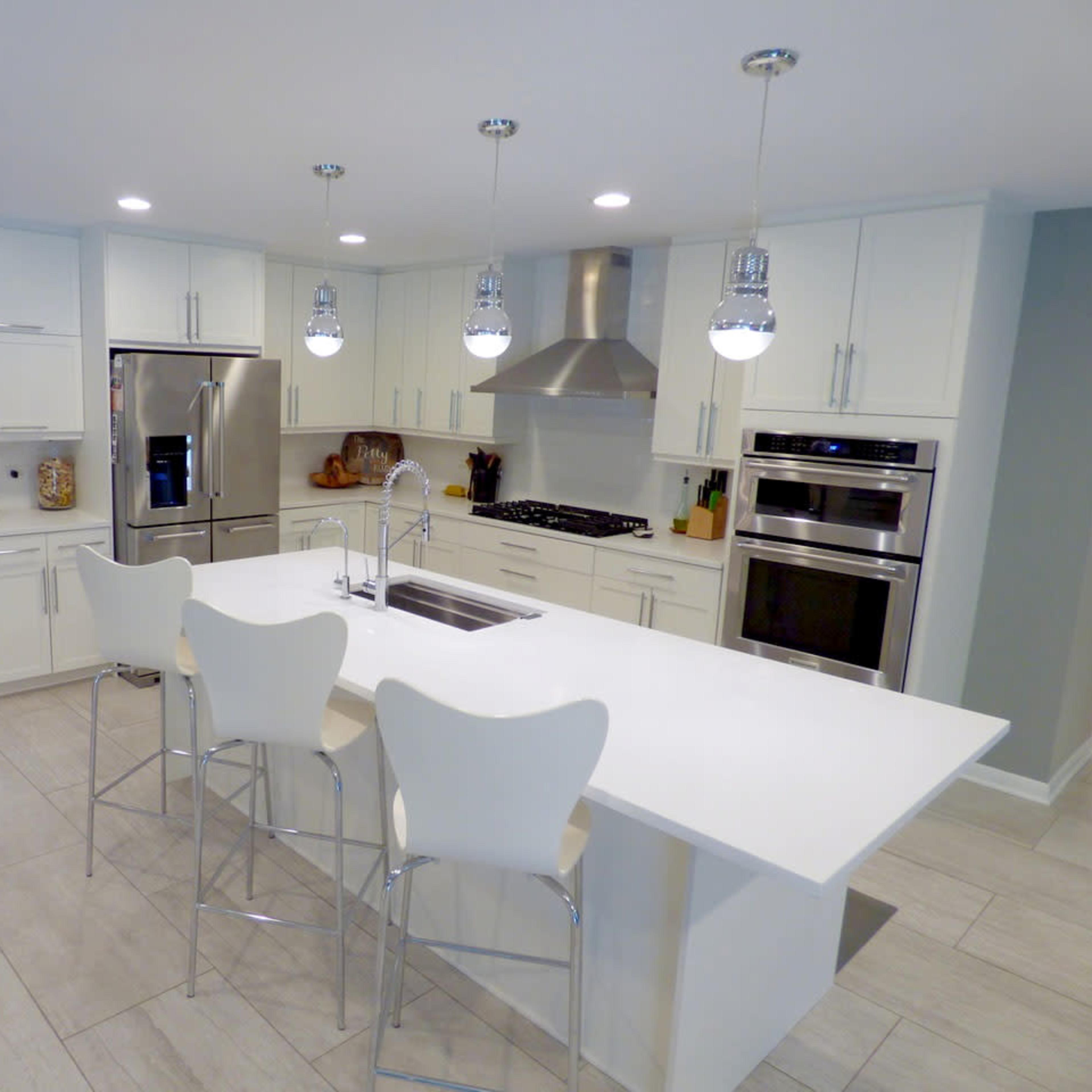 A modern kitchen features white cabinetry, stainless steel appliances, and a large island with seating.