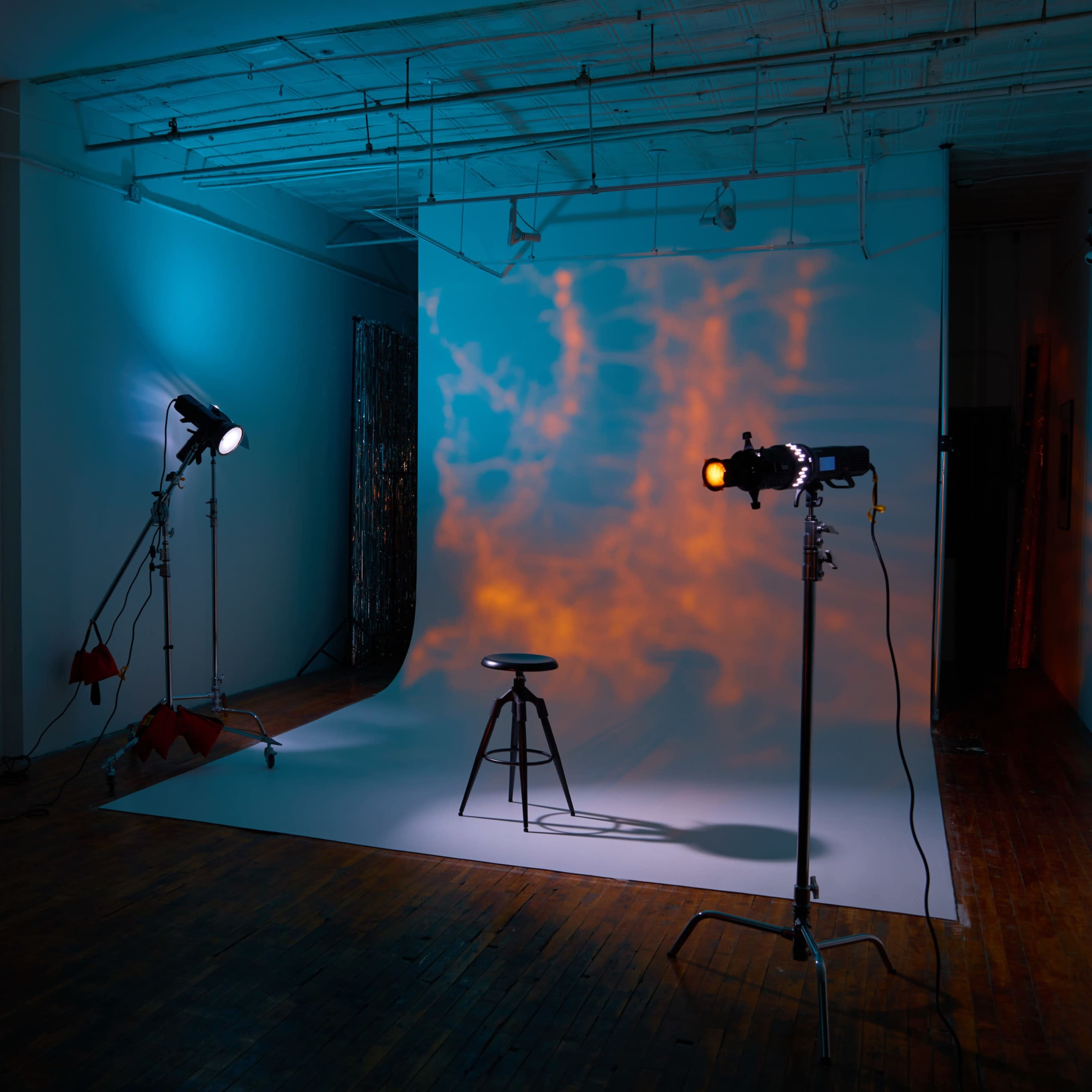 A photography studio with a stool positioned on a lit backdrop surrounded by various lighting equipment.