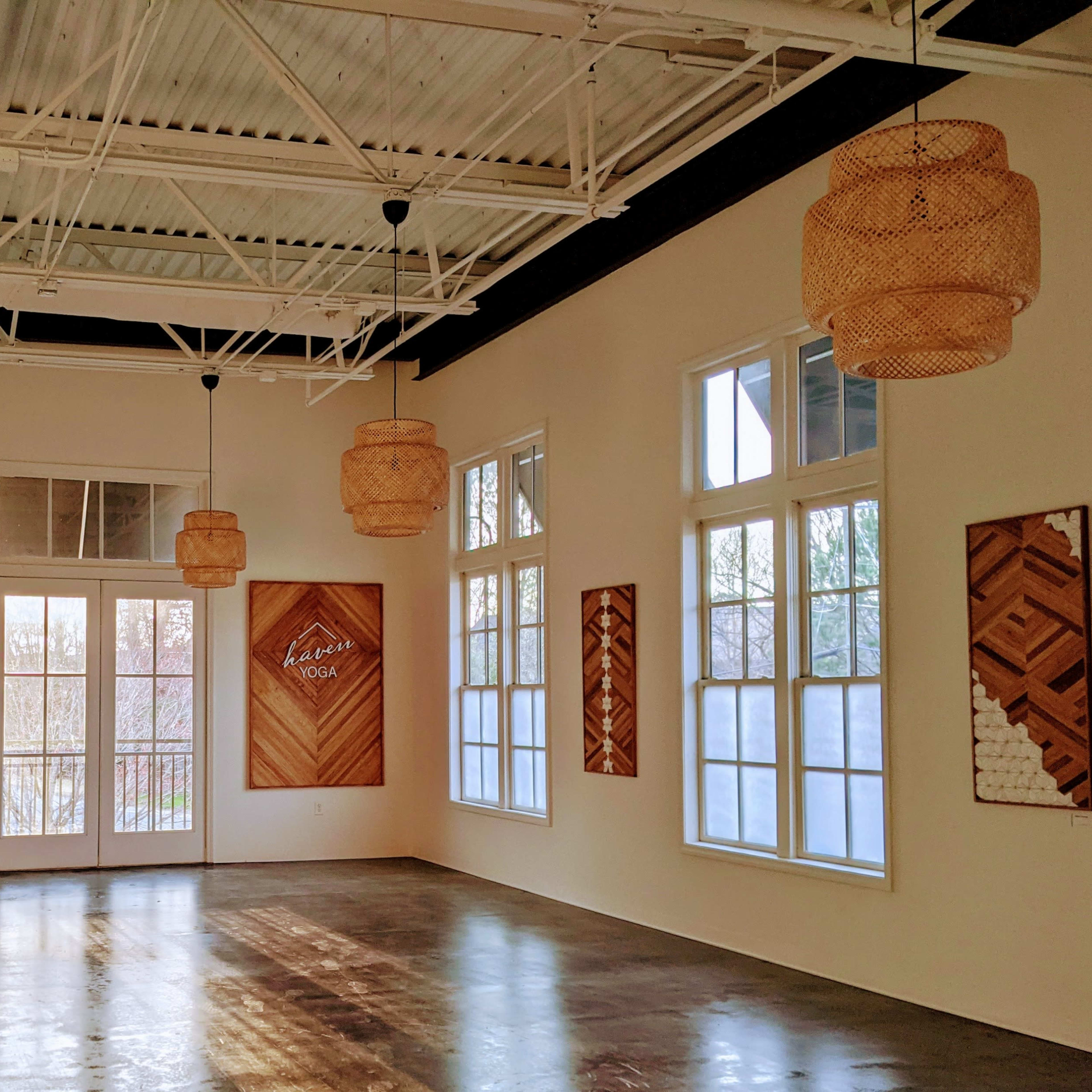 A spacious interior room with large windows, wooden wall decorations, and woven pendant lights hanging from the ceiling.