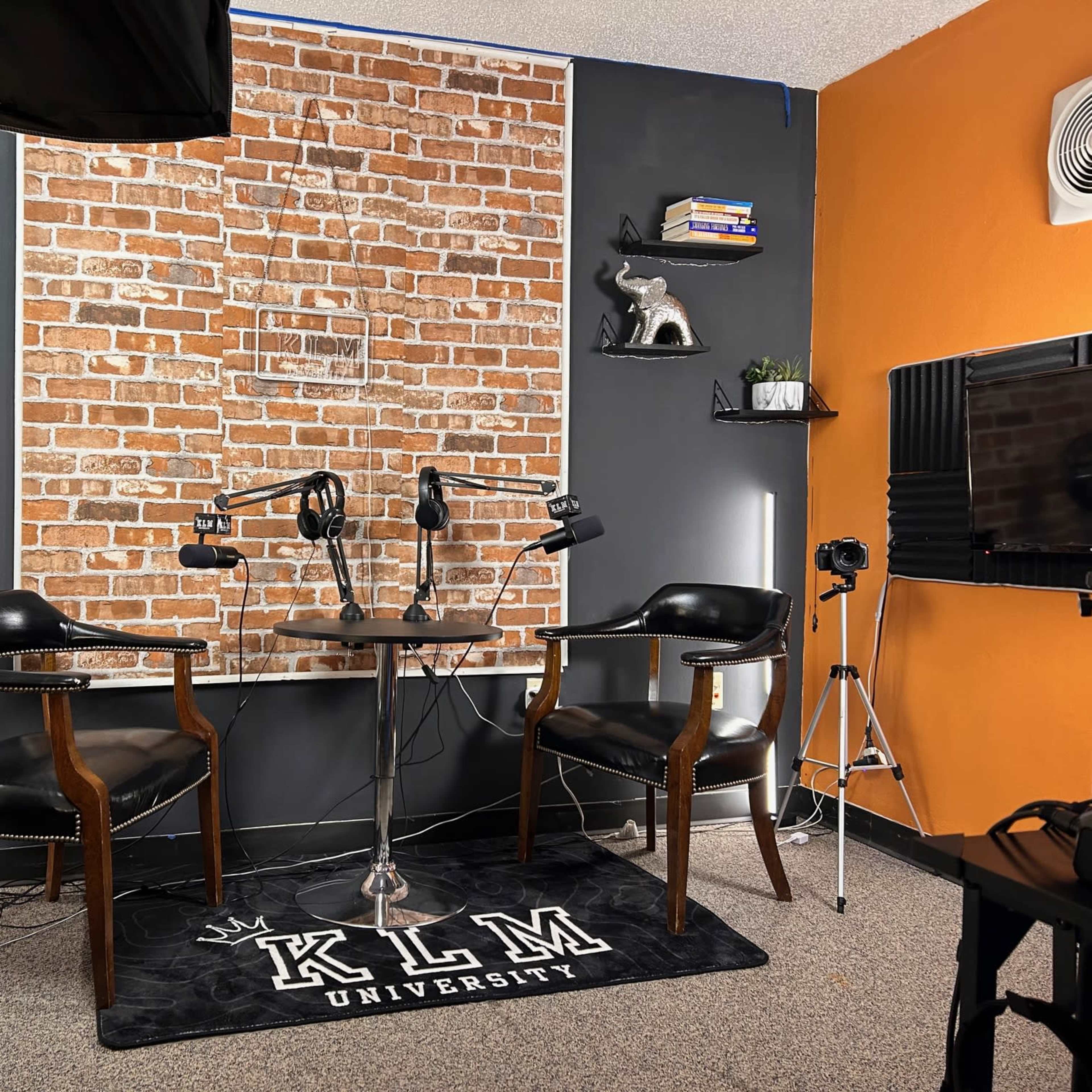 A podcast studio set with two chairs, a round table, and a brick wall backdrop, along with various lighting equipment and decorations.