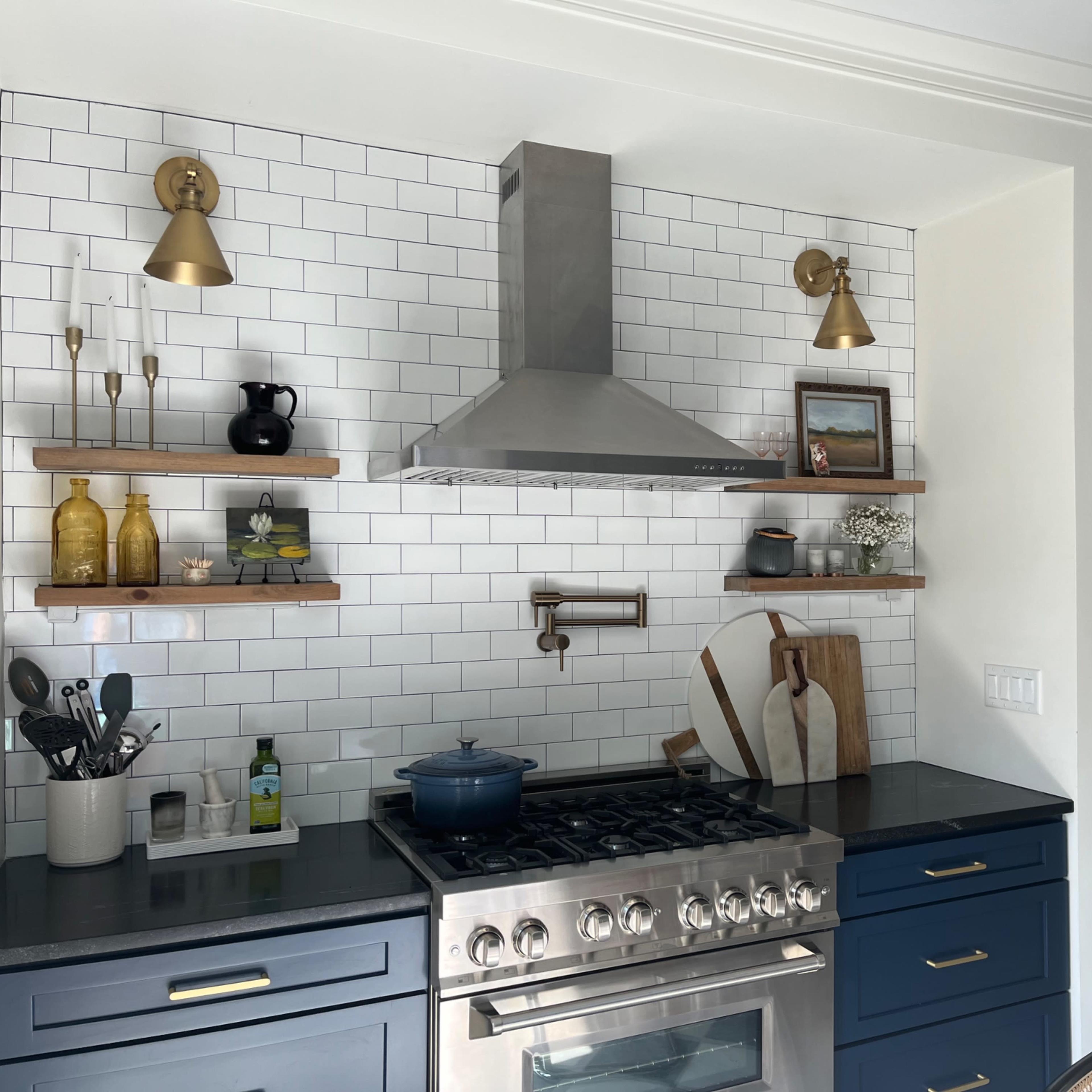 A modern kitchen with a stainless steel range hood, open shelving holding various kitchen items, and dark blue cabinetry.