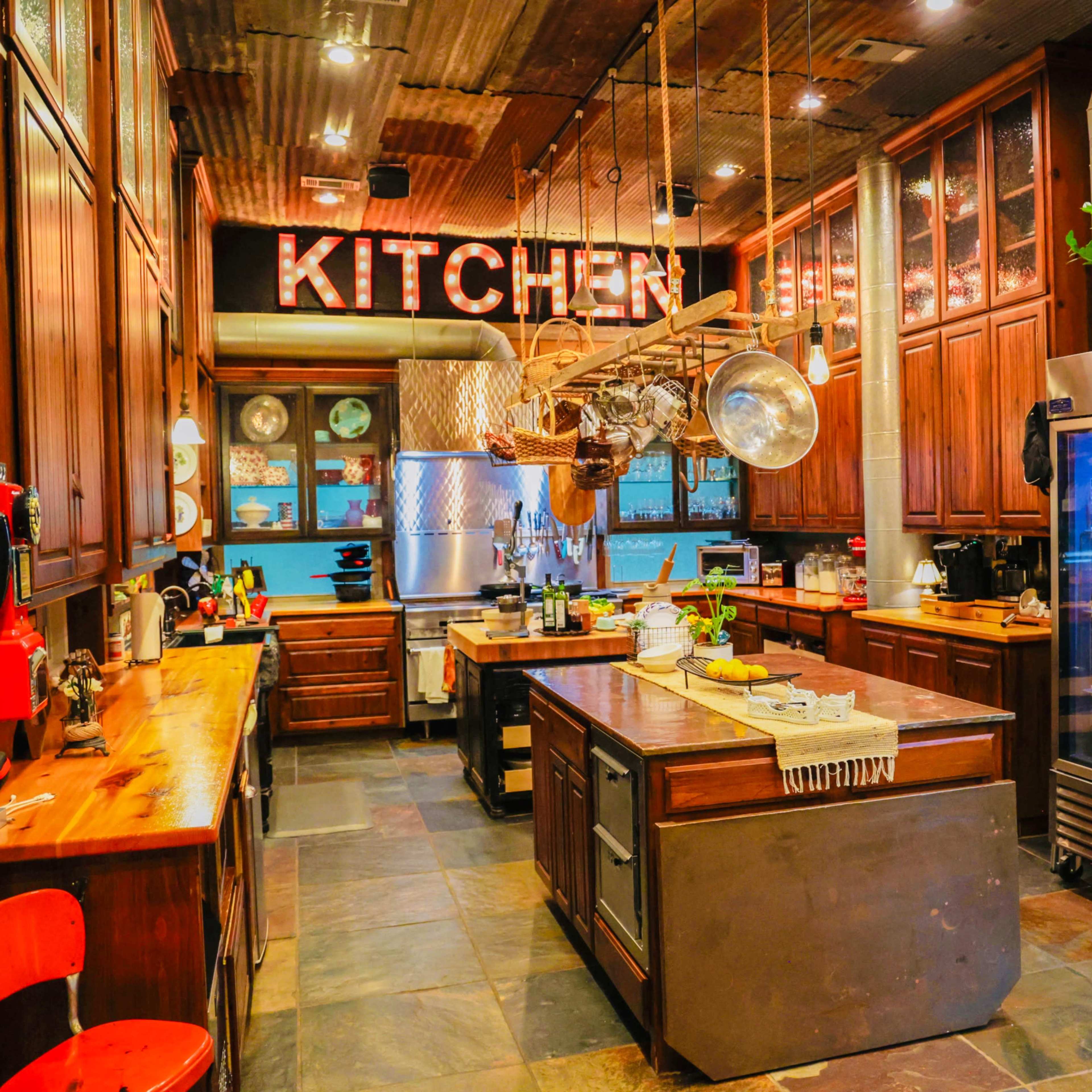 A rustic kitchen features wooden cabinets, a central island, and a large refrigerator beside a glass-fronted pantry.