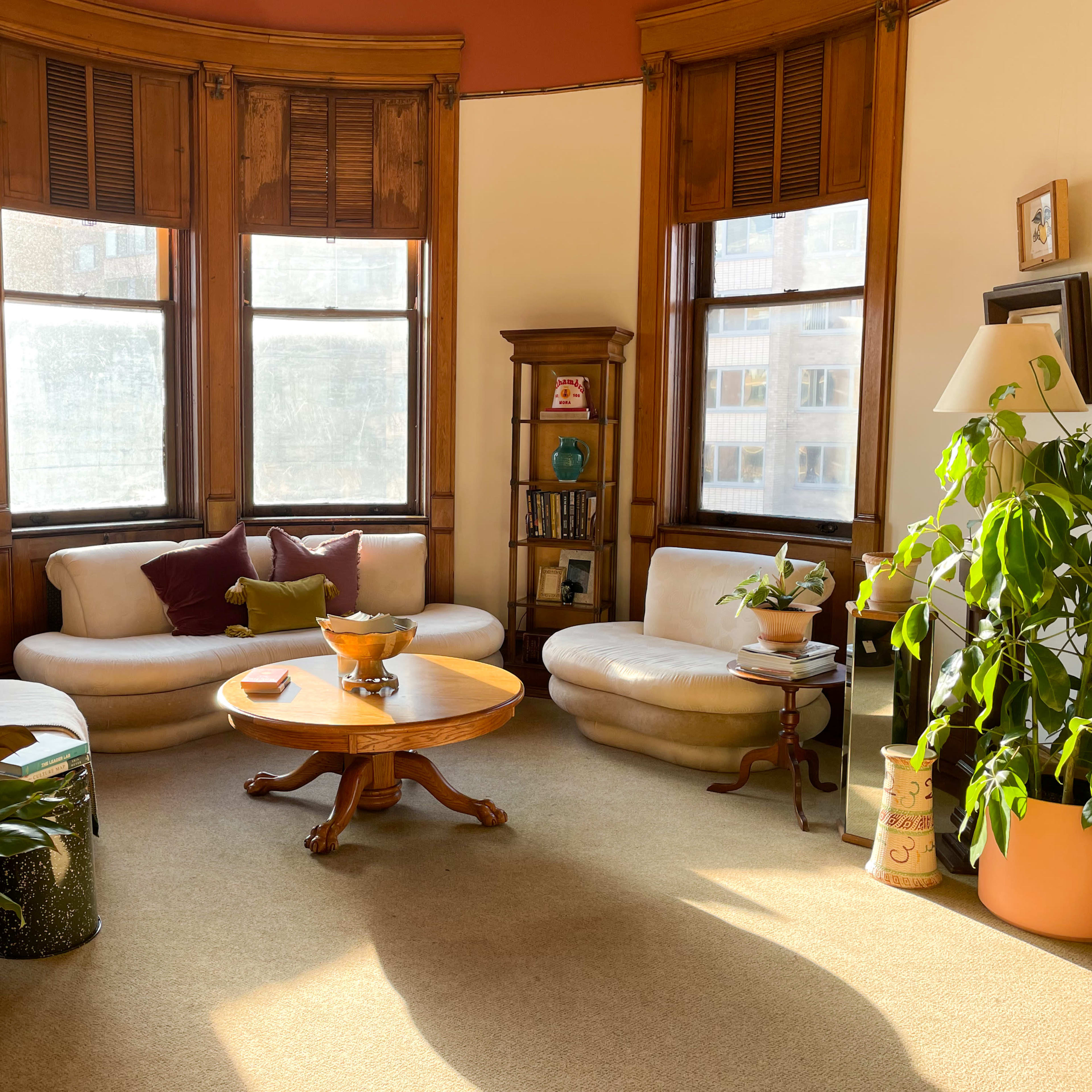A cozy living room with two curved sofas, a wooden coffee table, and large windows letting in natural light.