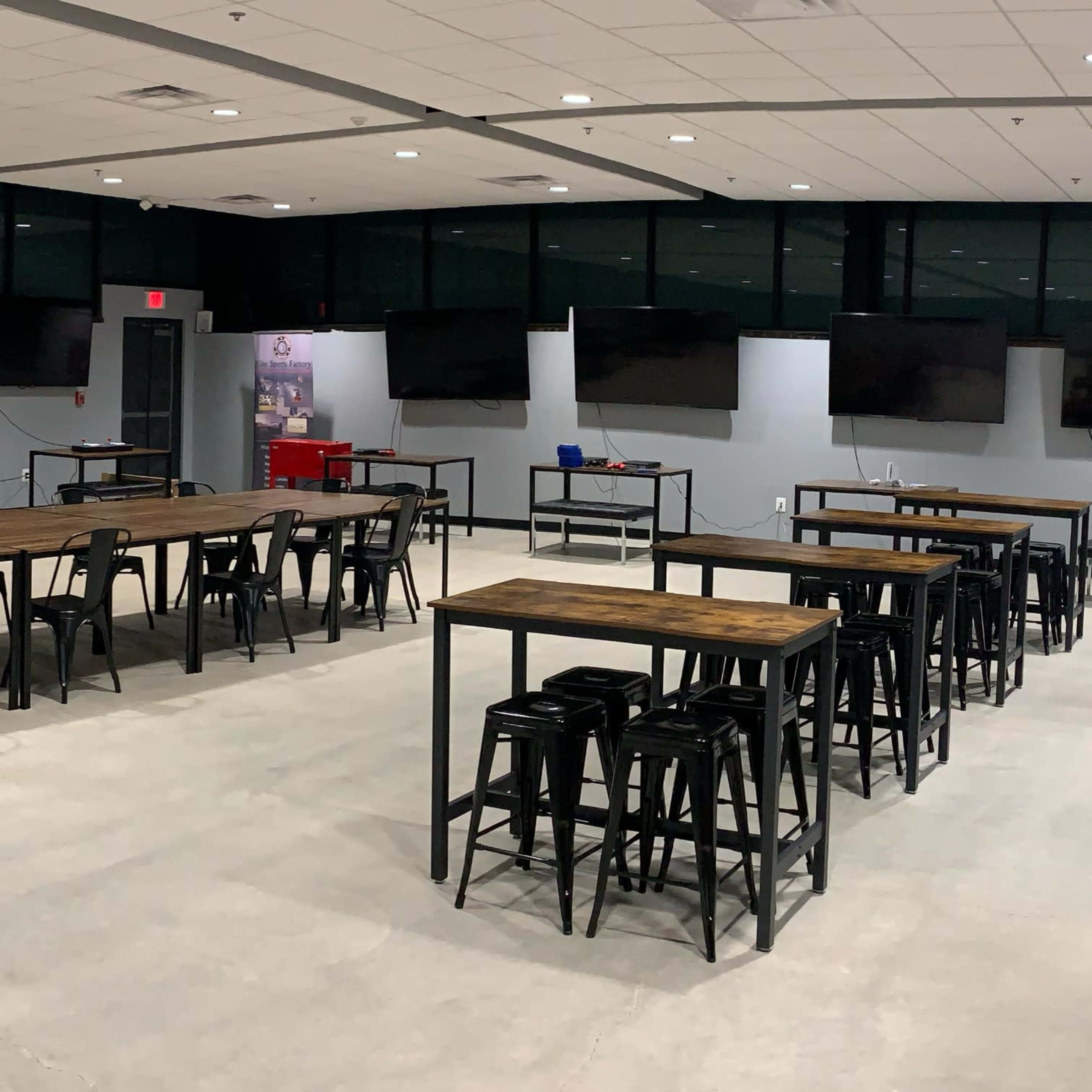 A spacious room with multiple long tables and high-backed stools, equipped with large screens mounted on the walls.