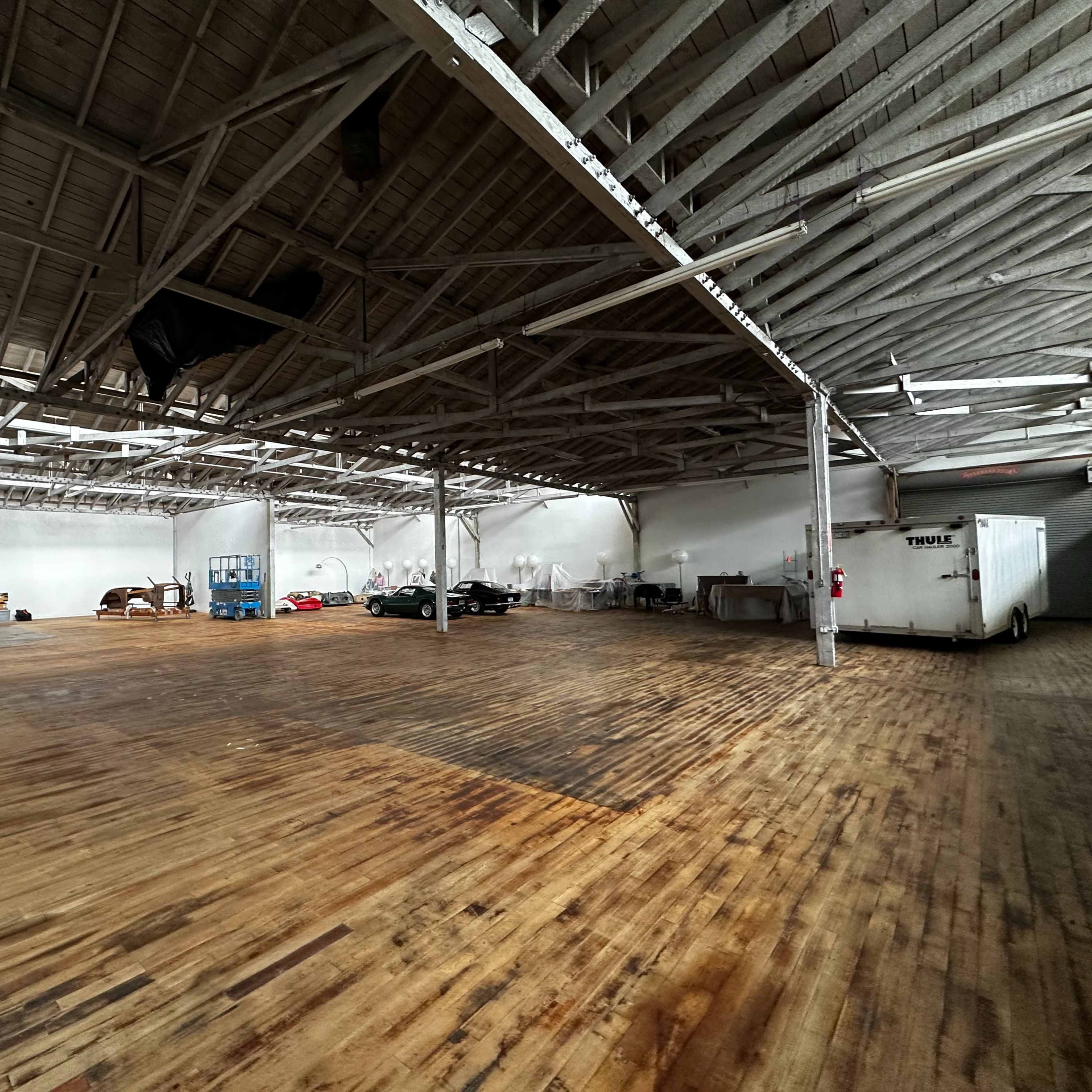 An empty industrial space with wooden floors, high ceilings, and various equipment along the walls.