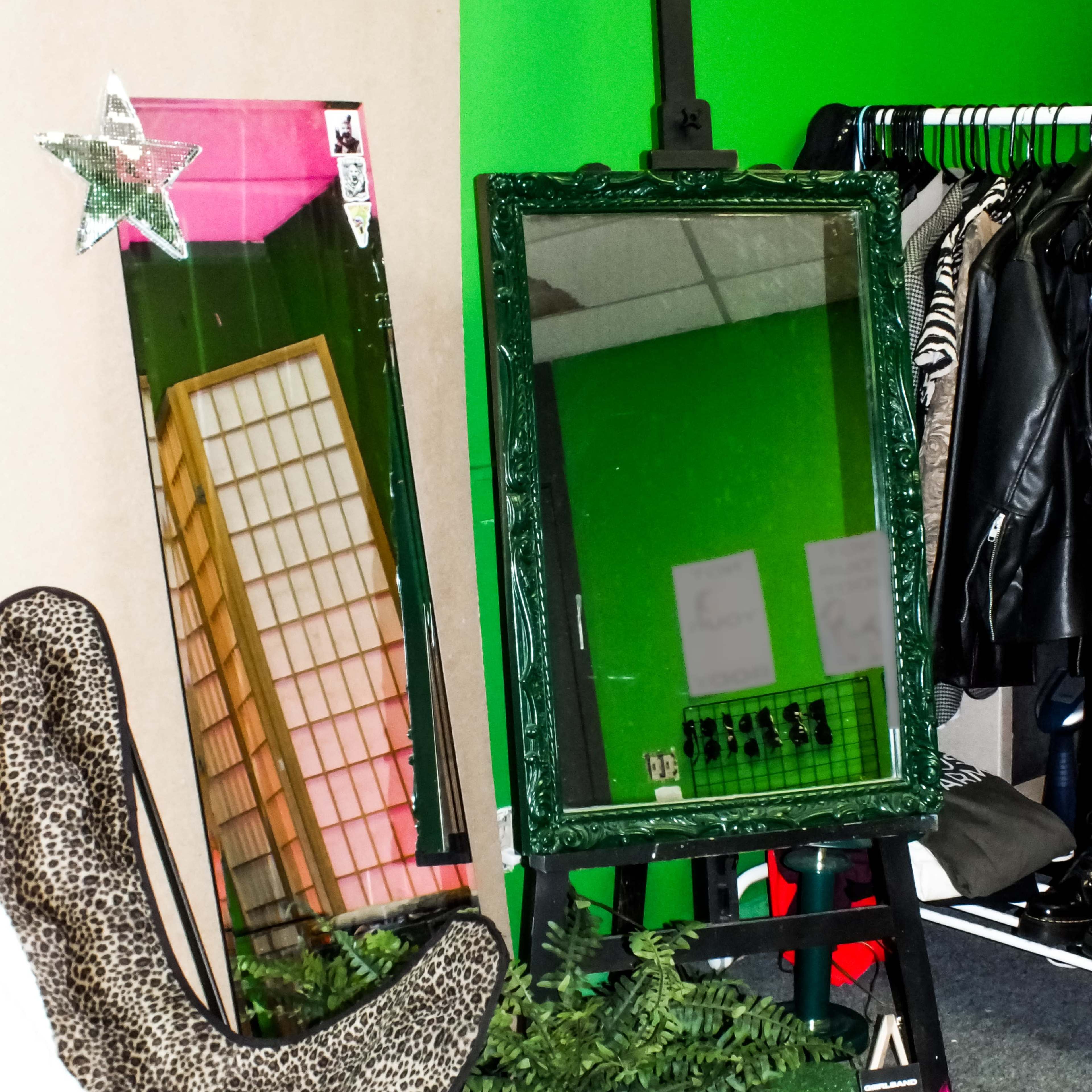 A mirror in a green frame leaning against a wall, alongside a tall, decorative panel and a chair with a leopard print design, all set in a space with green accents.