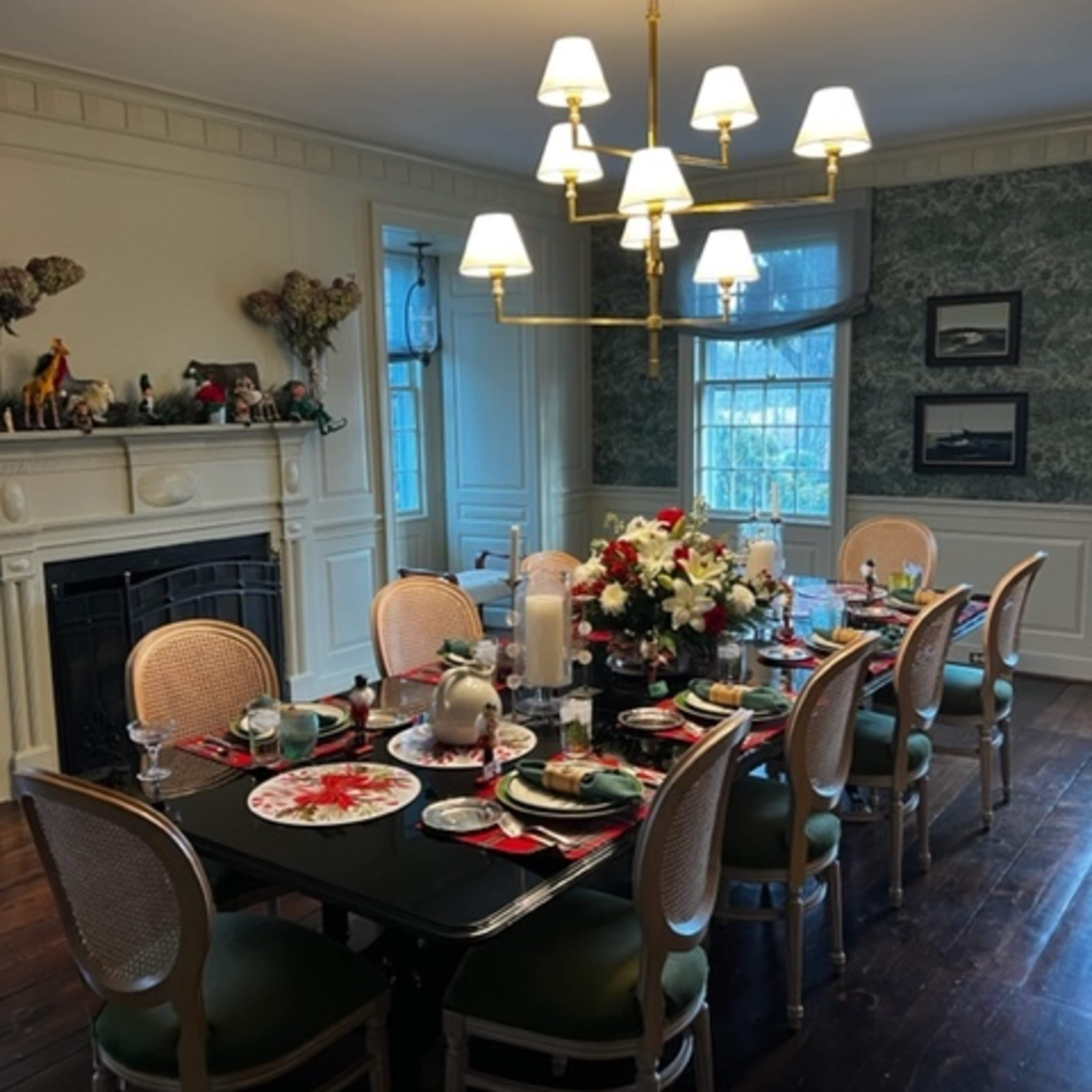 A large dining table is set for a meal, surrounded by chairs, with a floral centerpiece and a light fixture overhead in a well-decorated room.