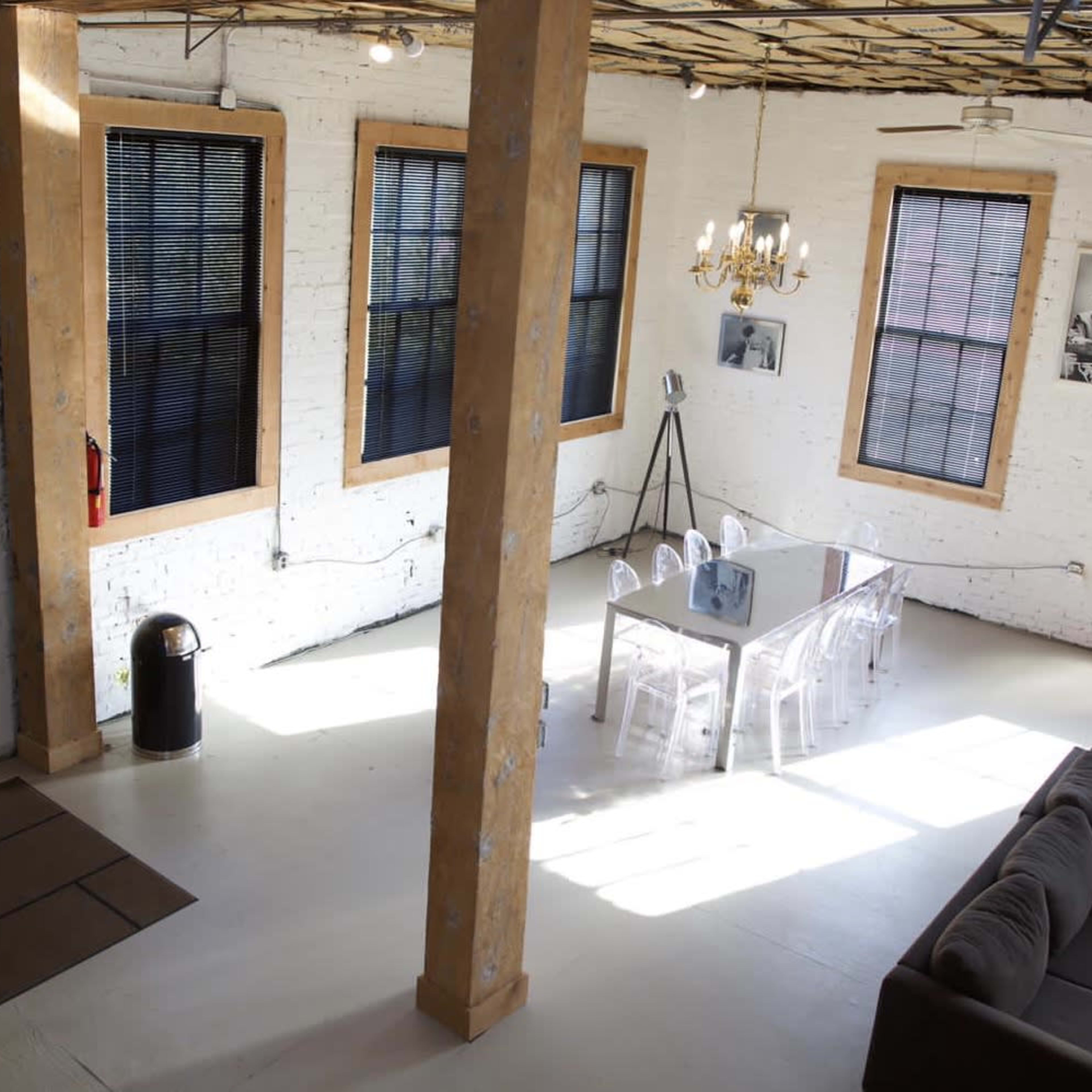 A spacious, modern interior with exposed brick walls, a dining table in the center, and large windows allowing natural light to enter.