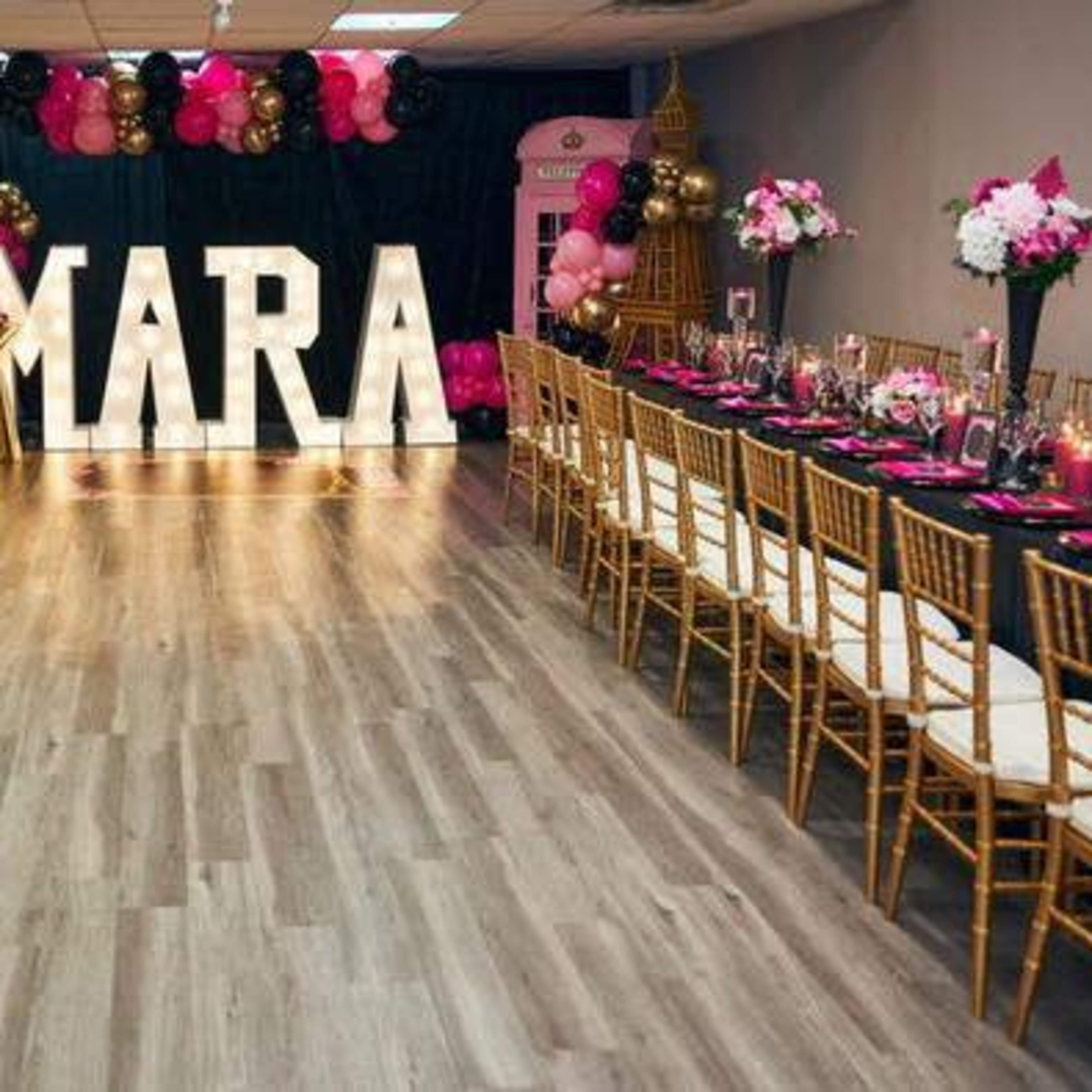 A decorated event space with a long dining setup featuring floral centerpieces and large illuminated letters spelling "MARA."