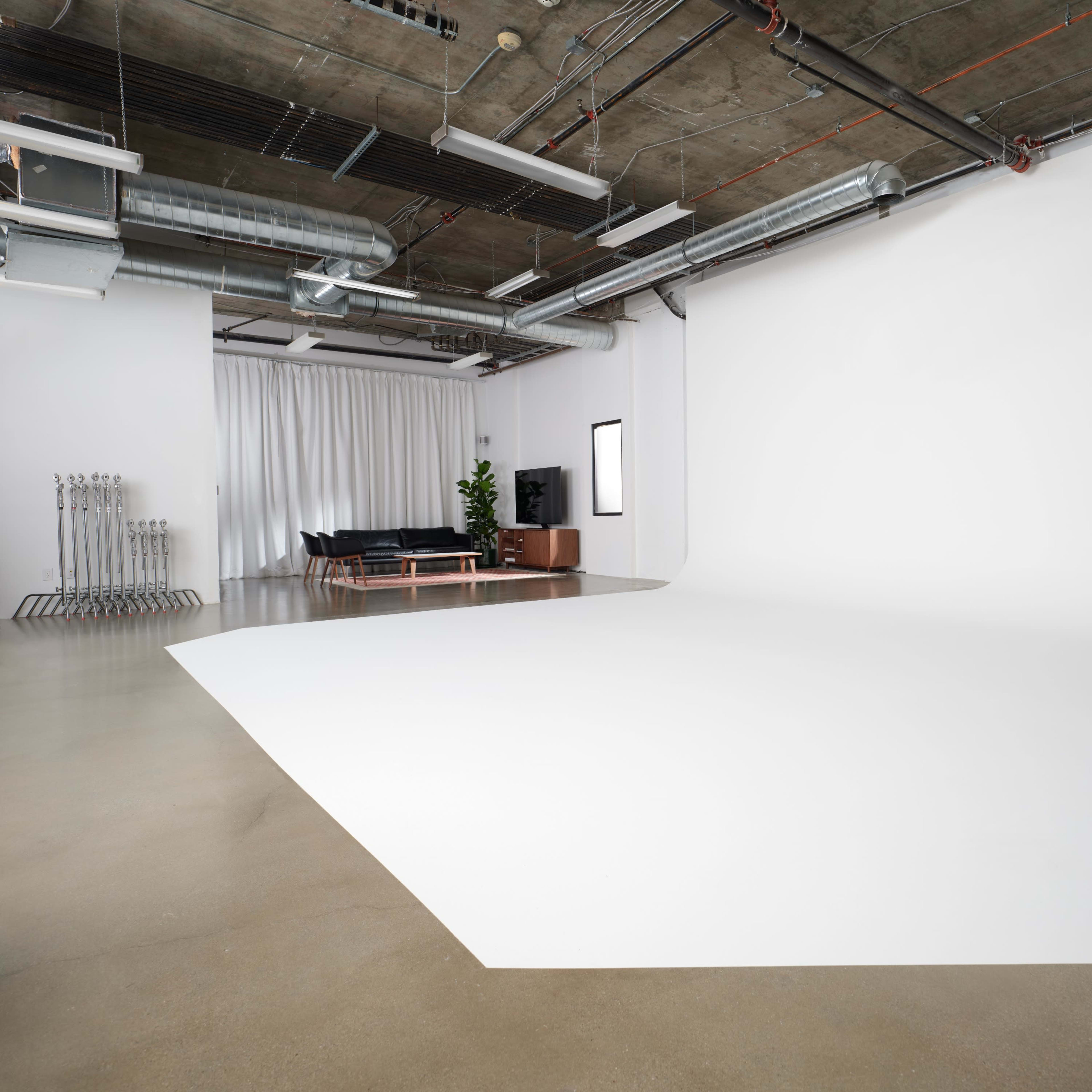 A large, minimalistic studio space with a seamless white backdrop, polished concrete floors, and a black sofa in one corner.