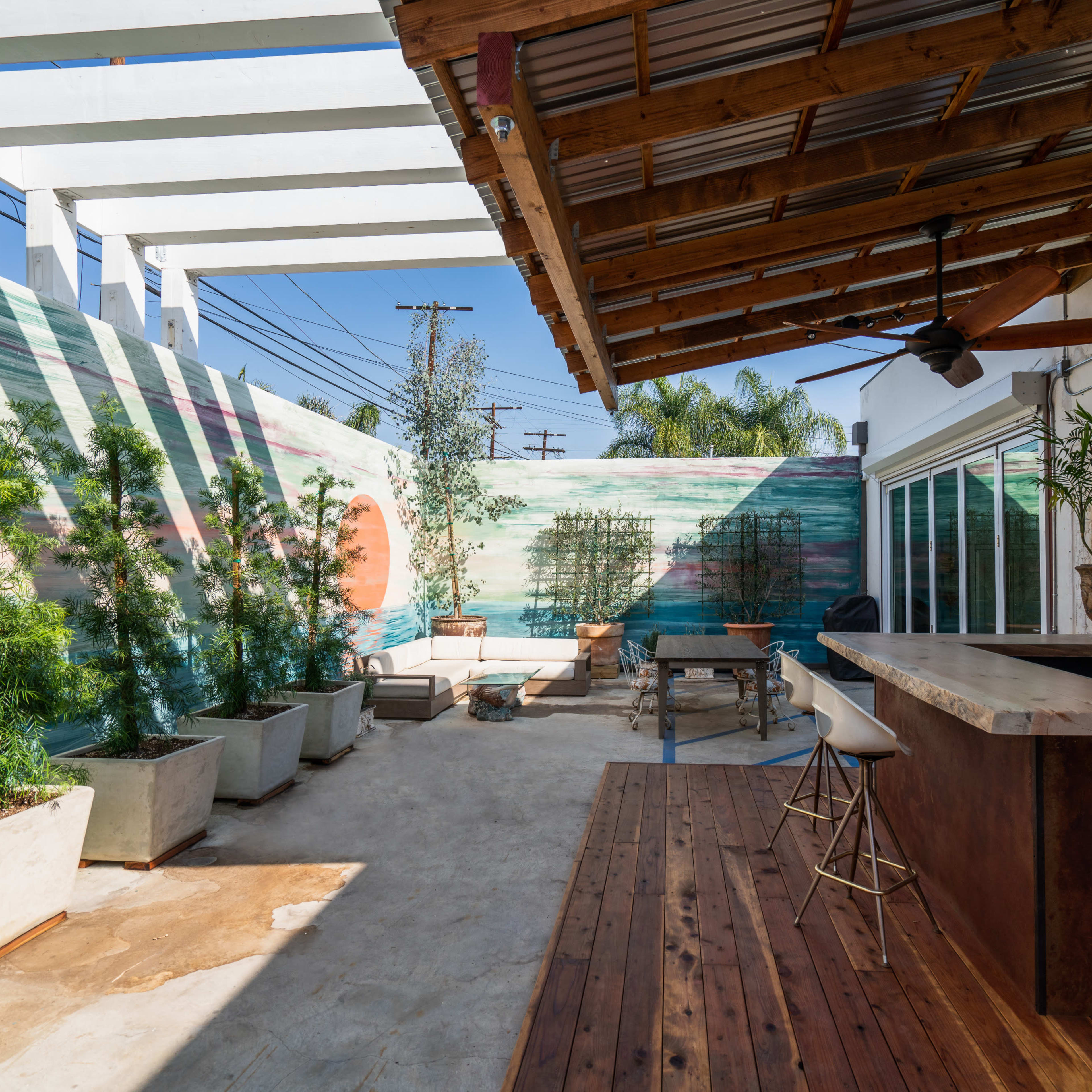 An outdoor patio area with a wooden bar, planters, and a colorful mural on the wall.