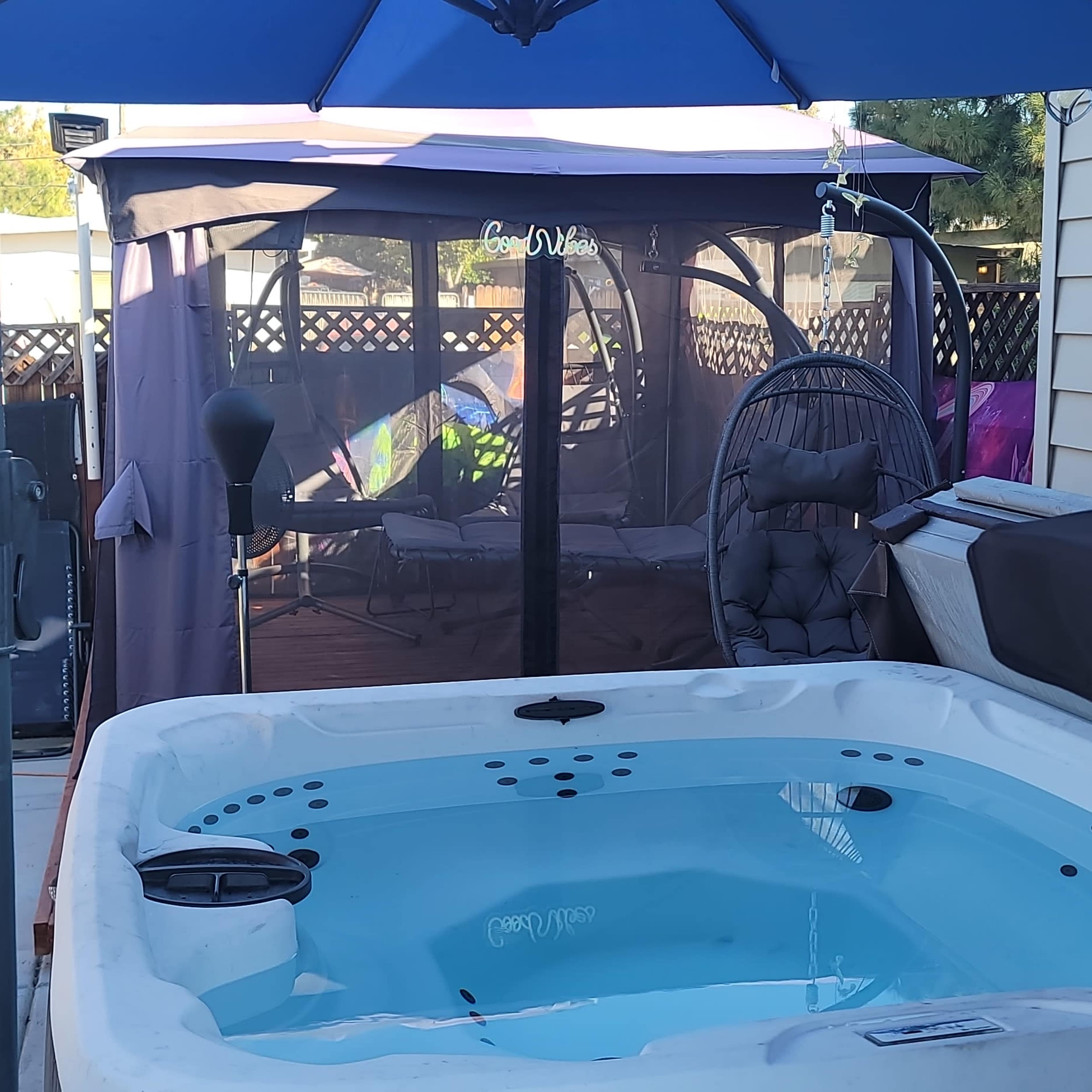A hot tub beside a shaded sitting area with a canopy and hanging chair in a backyard setting.