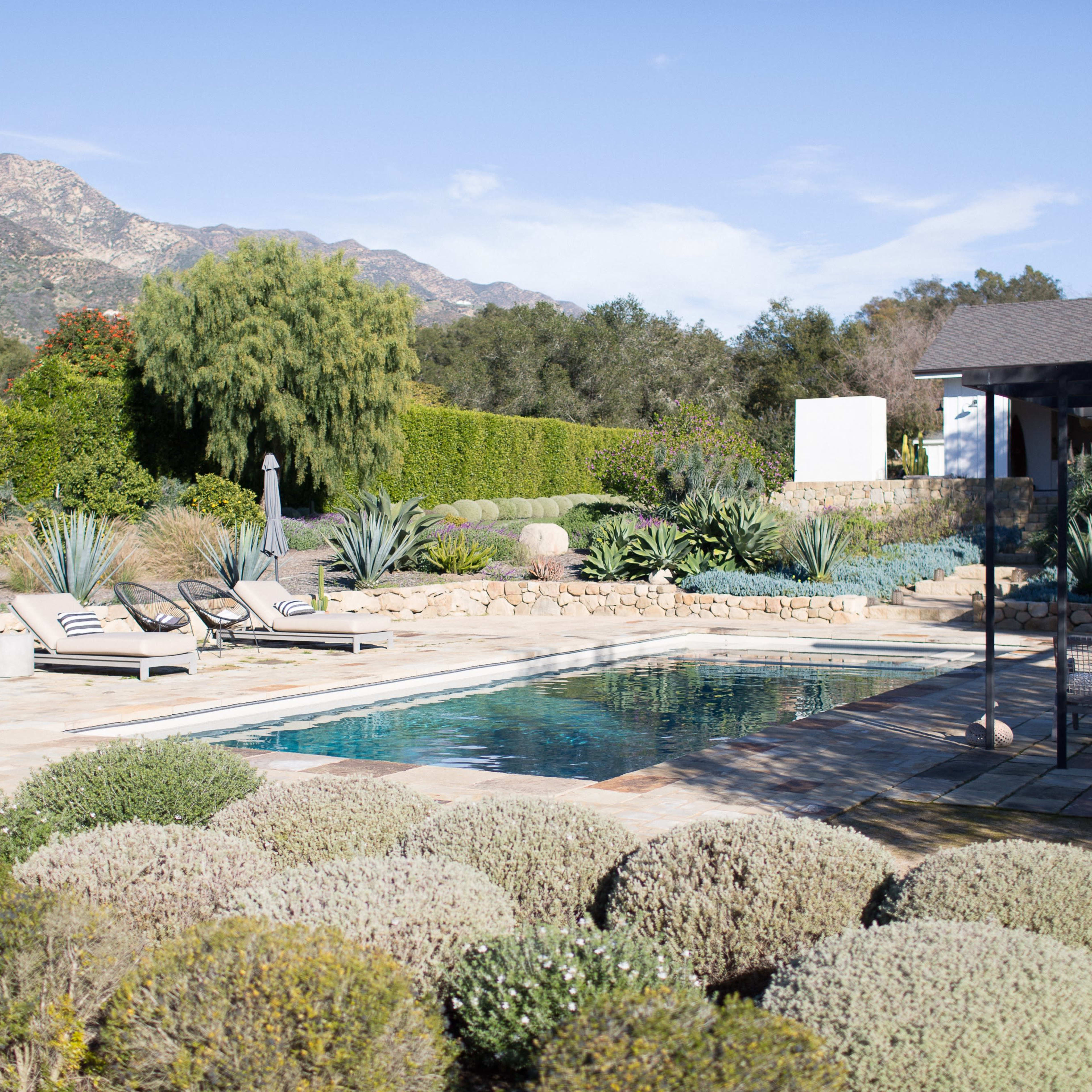 A swimming pool is surrounded by landscaped gardens, loungers, and mountains in the background.