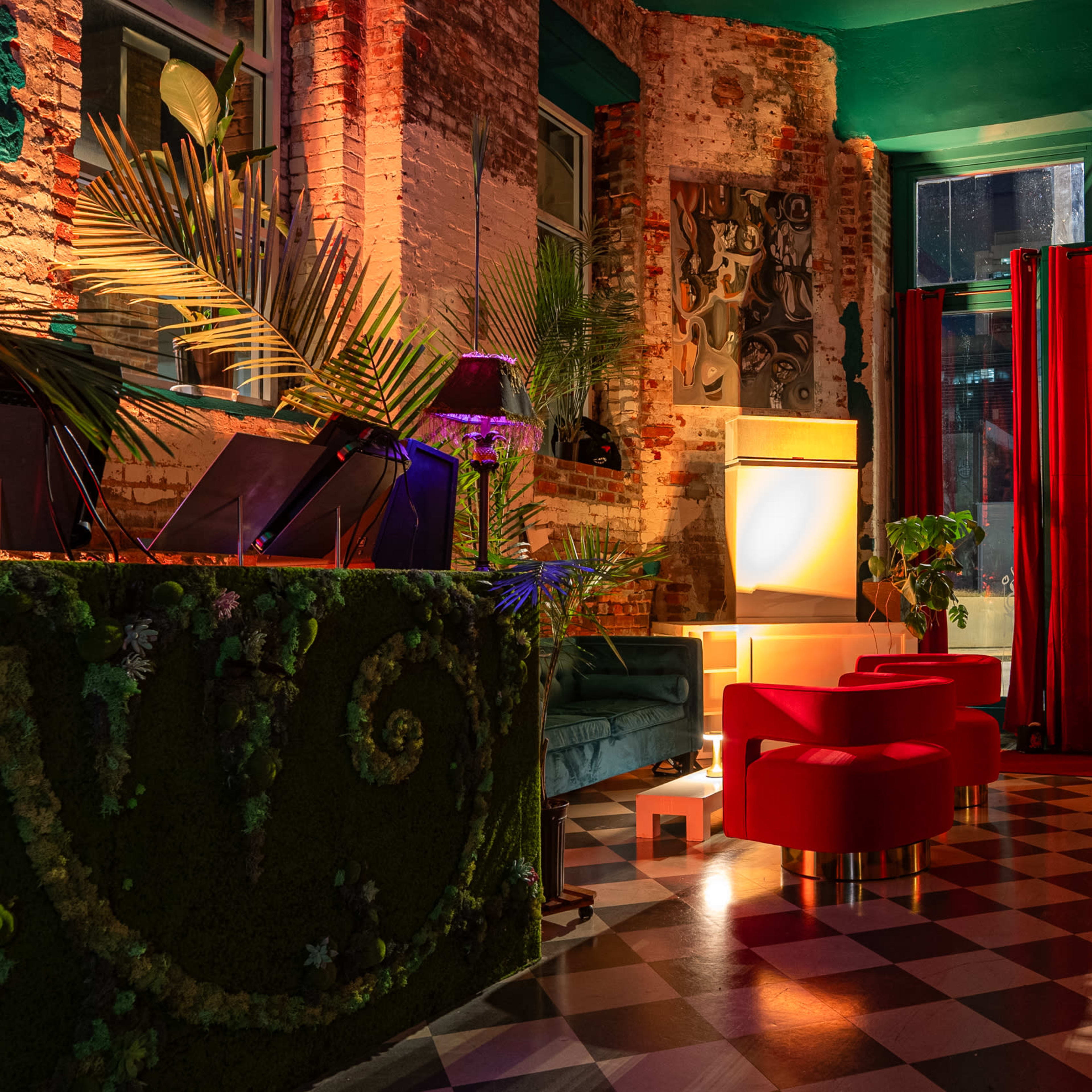 The scene shows a stylish lounge with red curtains, modern seating, plants, and patterned flooring, illuminated by soft lighting.