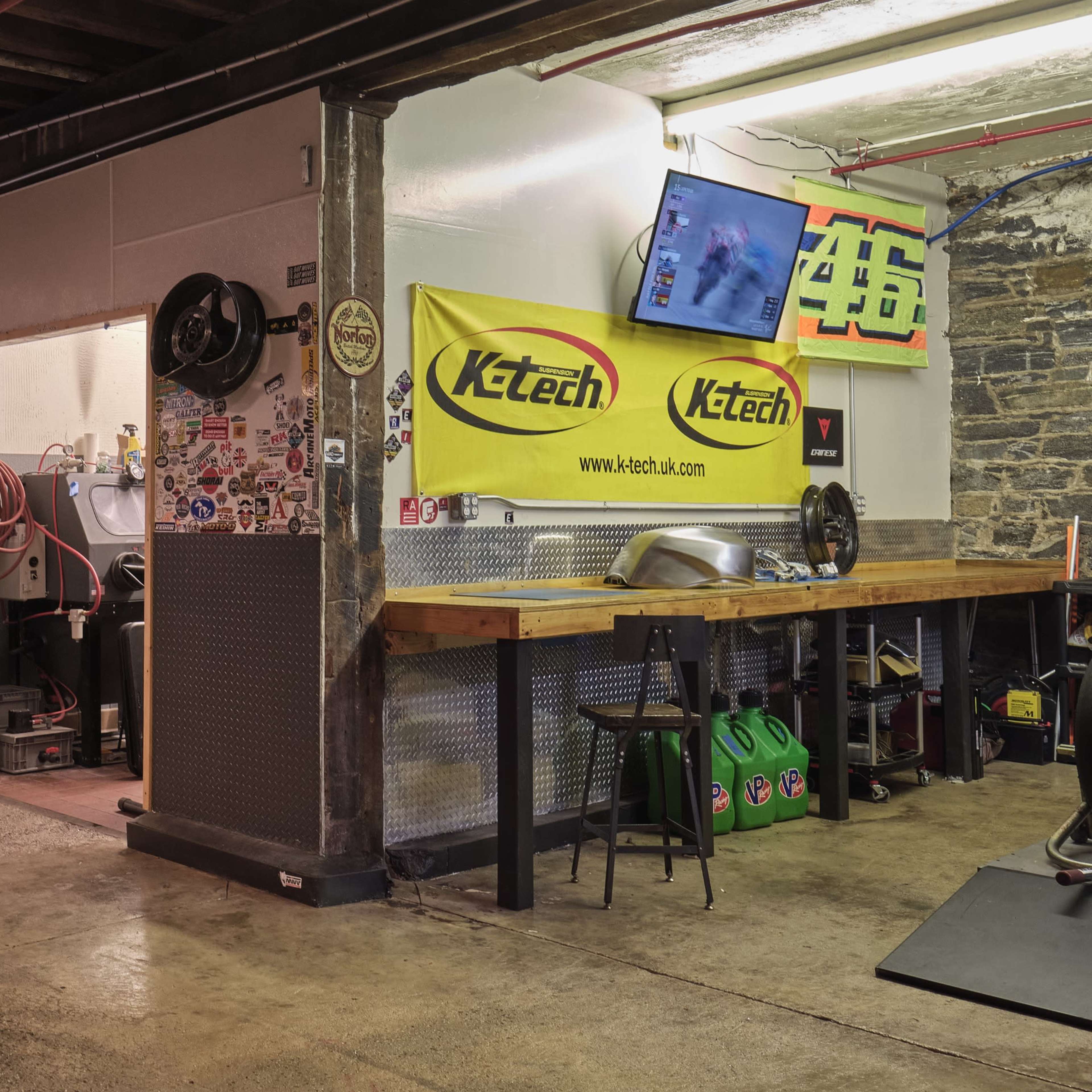 A spacious, industrial-style workshop with exposed brick walls, a counter, and various equipment, including monitors and banners.