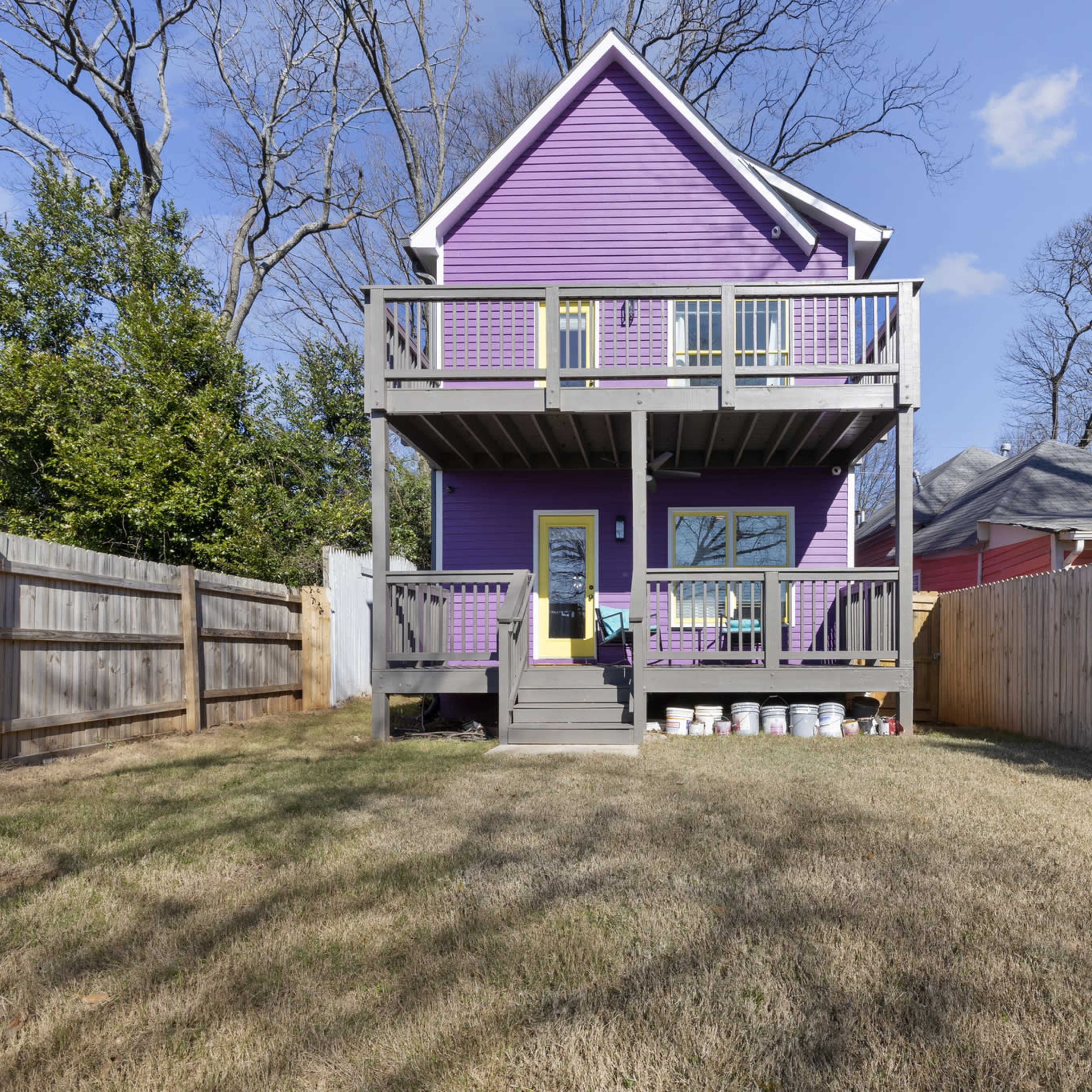 A purple two-story house with a front porch and a grass yard is surrounded by wooden fences.