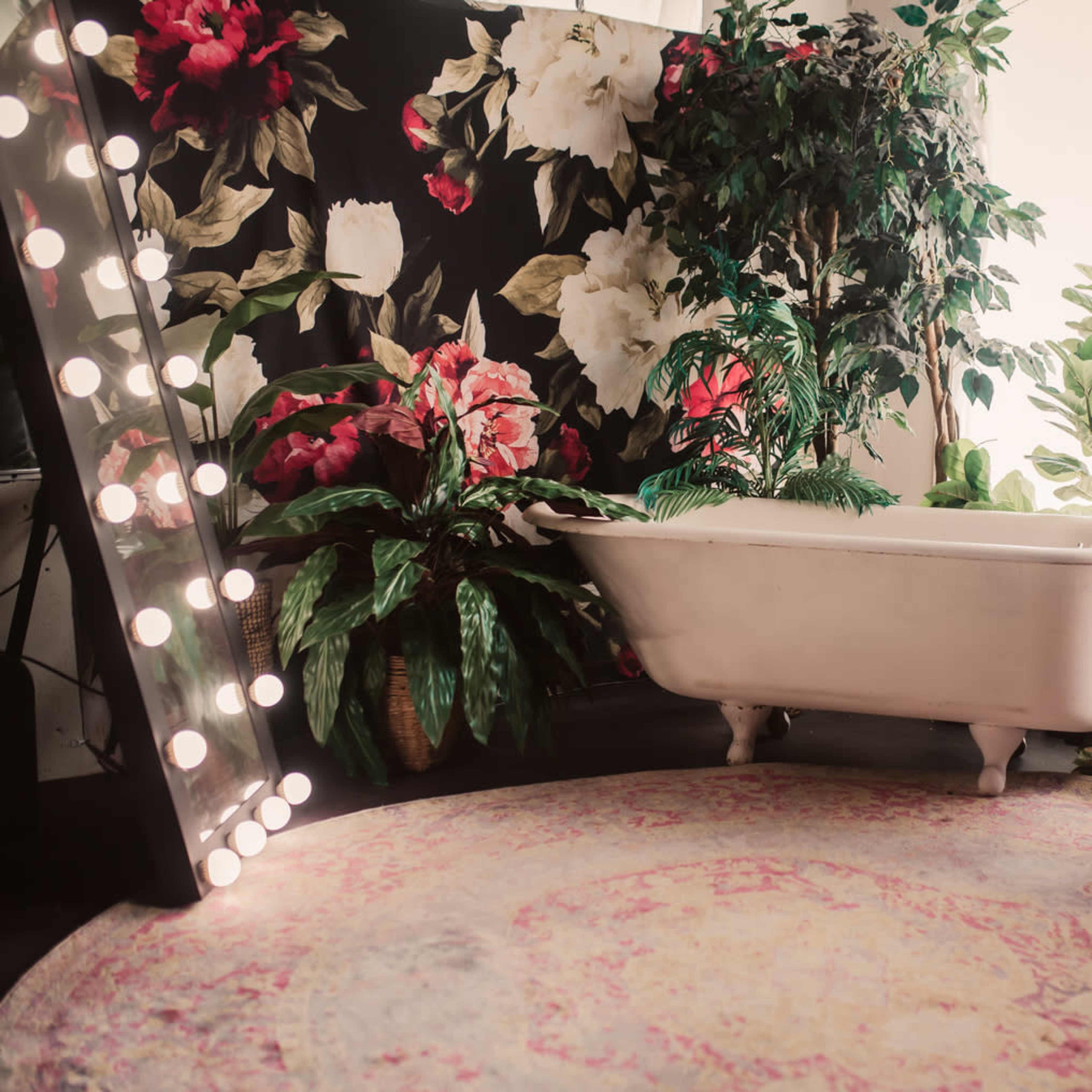 A vintage white bathtub alongside a lush backdrop of flowers, a rattan chair, and decorative plants in a cozy interior space.
