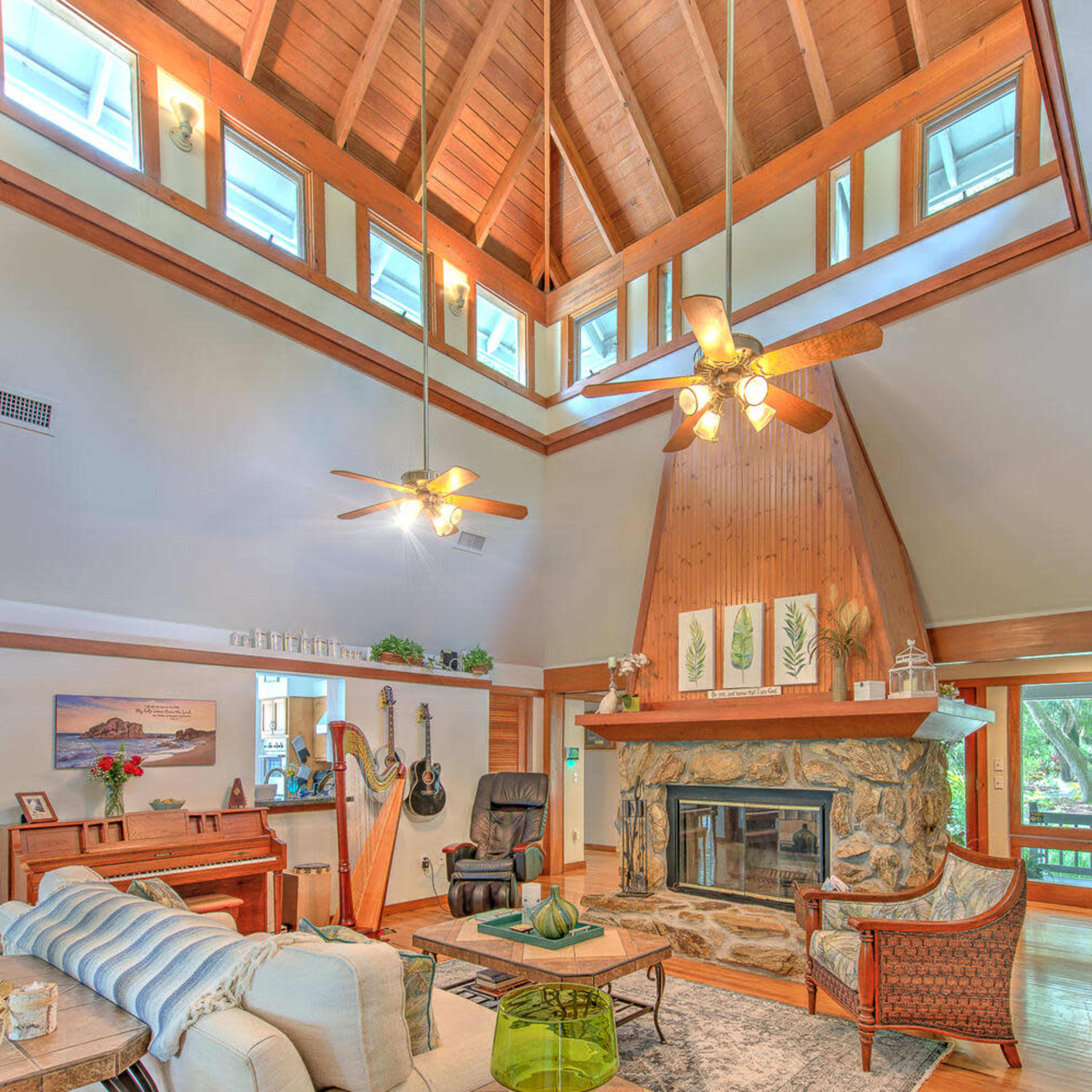 The living room features a high, wooden-beamed ceiling, a stone fireplace, and large windows overlooking a garden.