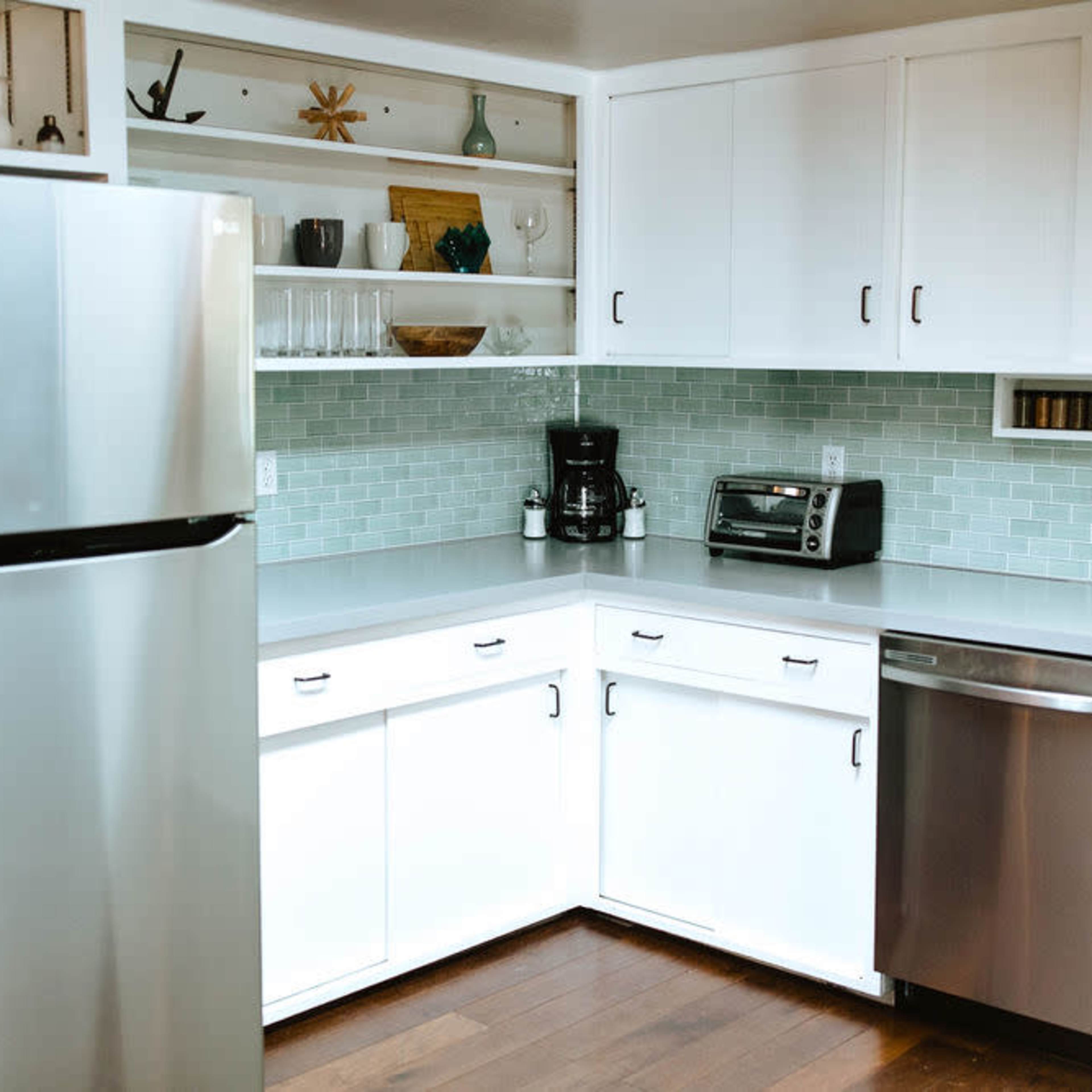 A modern kitchen with stainless steel appliances, white cabinetry, and light green tiled backsplash.
