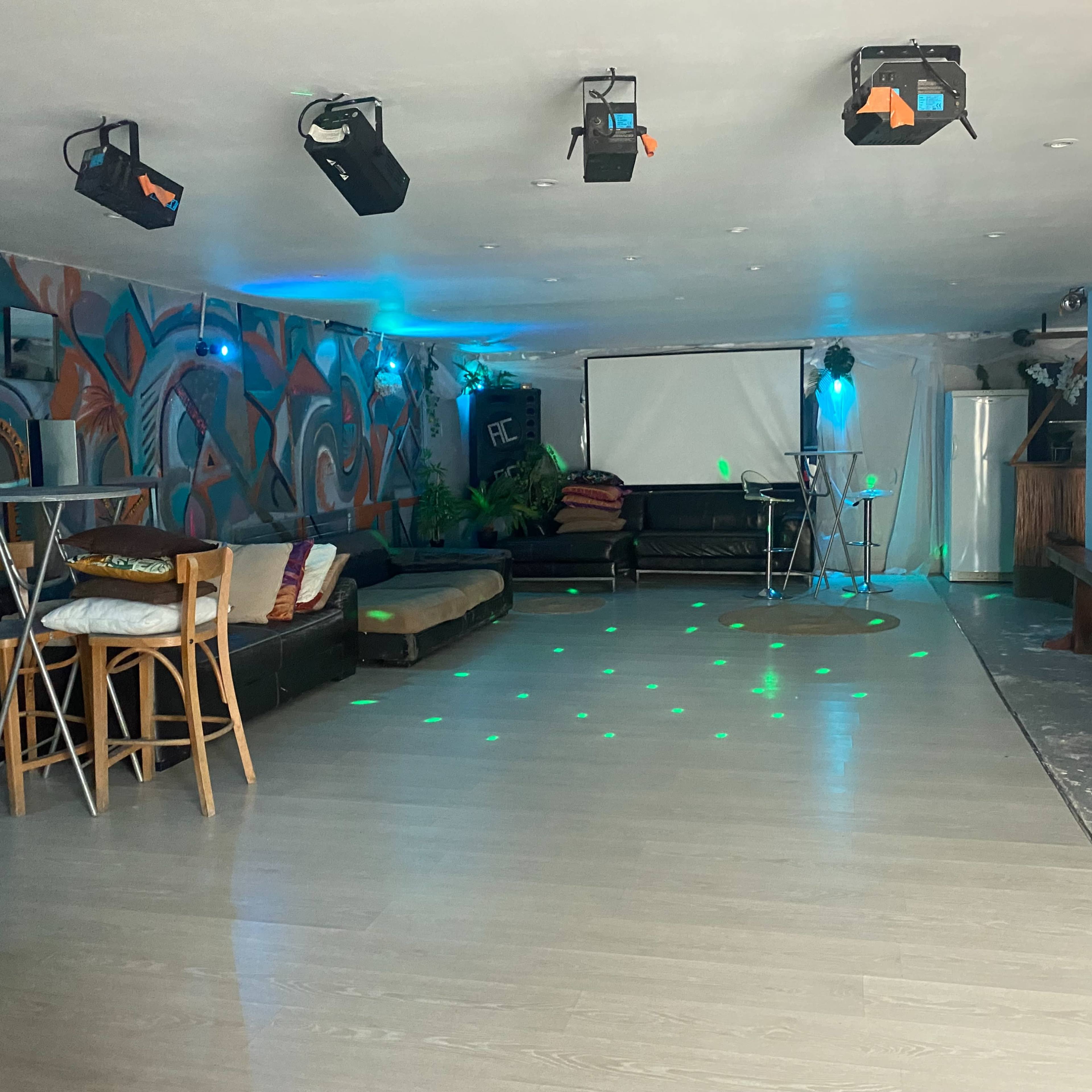 An empty lounge area with a dance floor, low seating, and colorful lighting.
