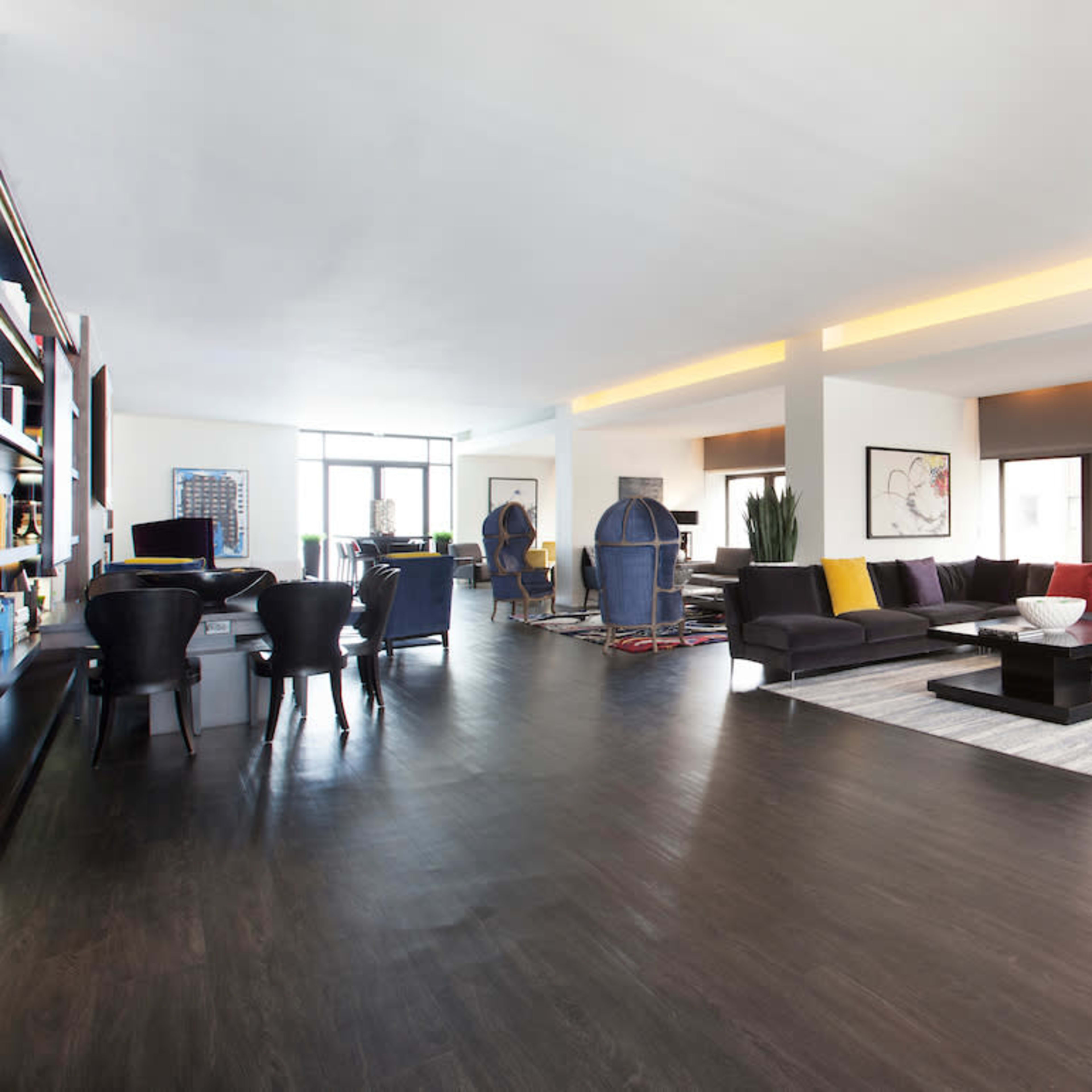 A modern living space features a sectional sofa with colorful cushions, large windows, and a dining area with black chairs.