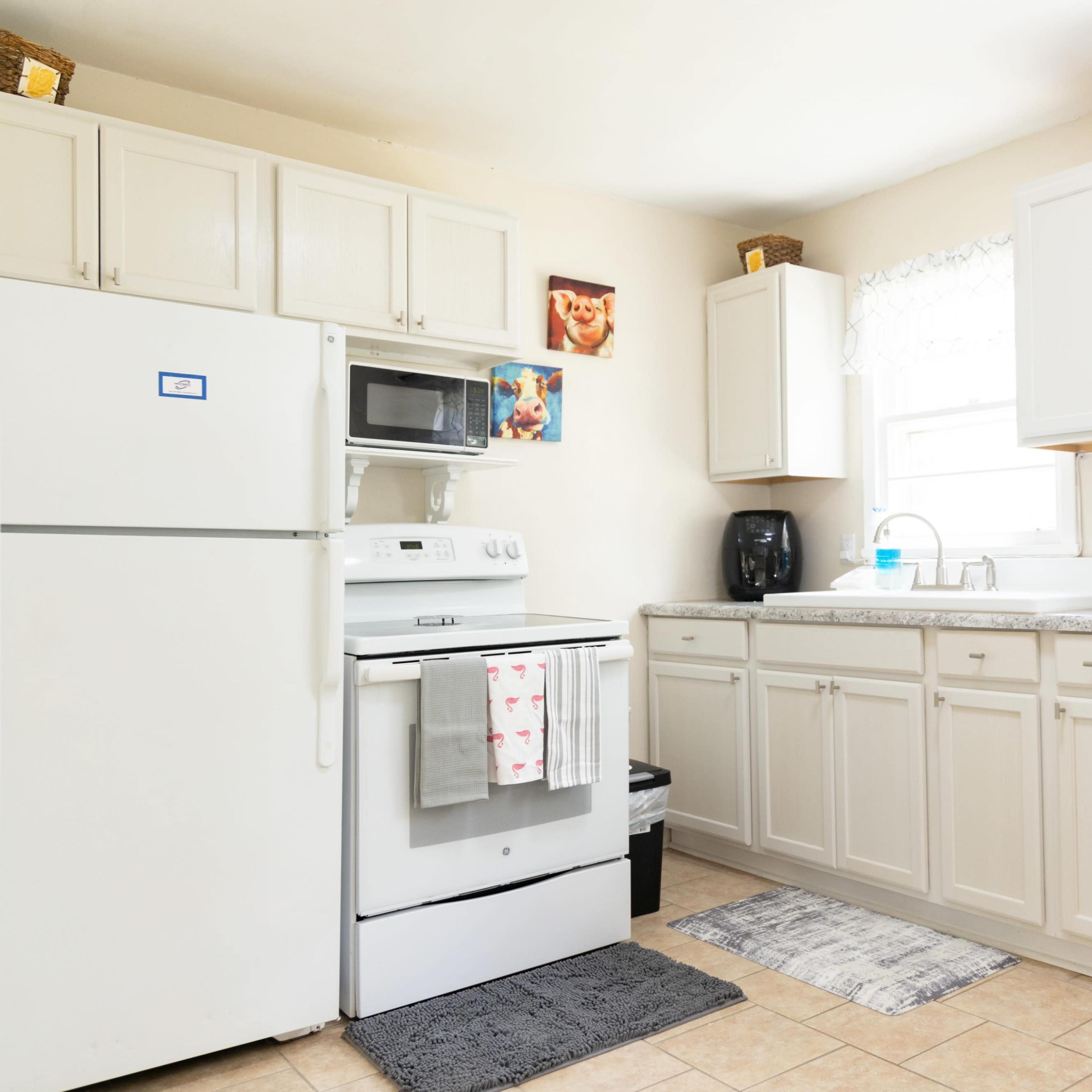 A modern kitchen with white cabinets, a refrigerator, and a stove, featuring a sink and various kitchen appliances on the counter.
